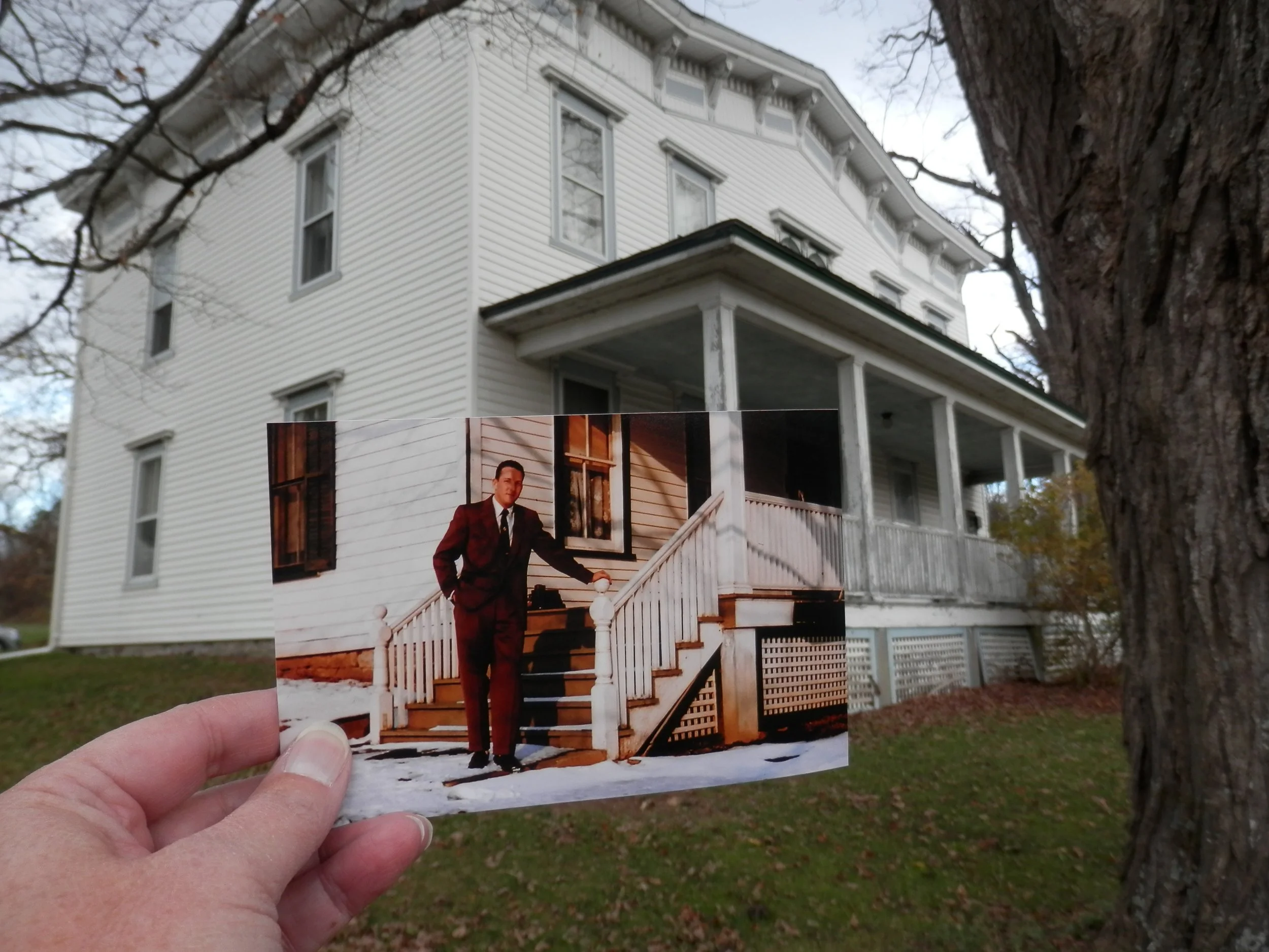 a photograph of a man standing at the base of porch steps, in front of the actual house