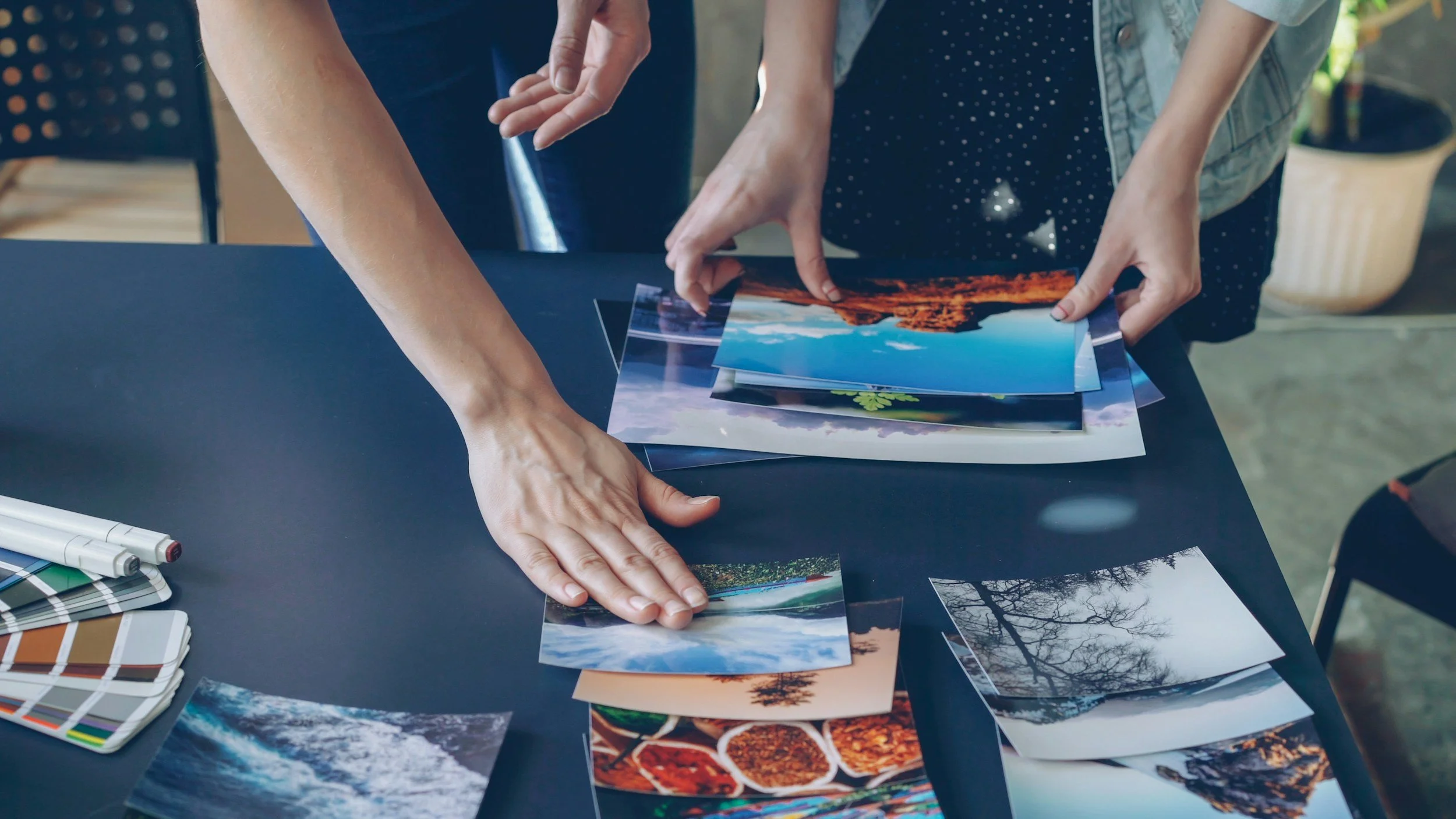 two people organizing photos that are laid out on a tabletop