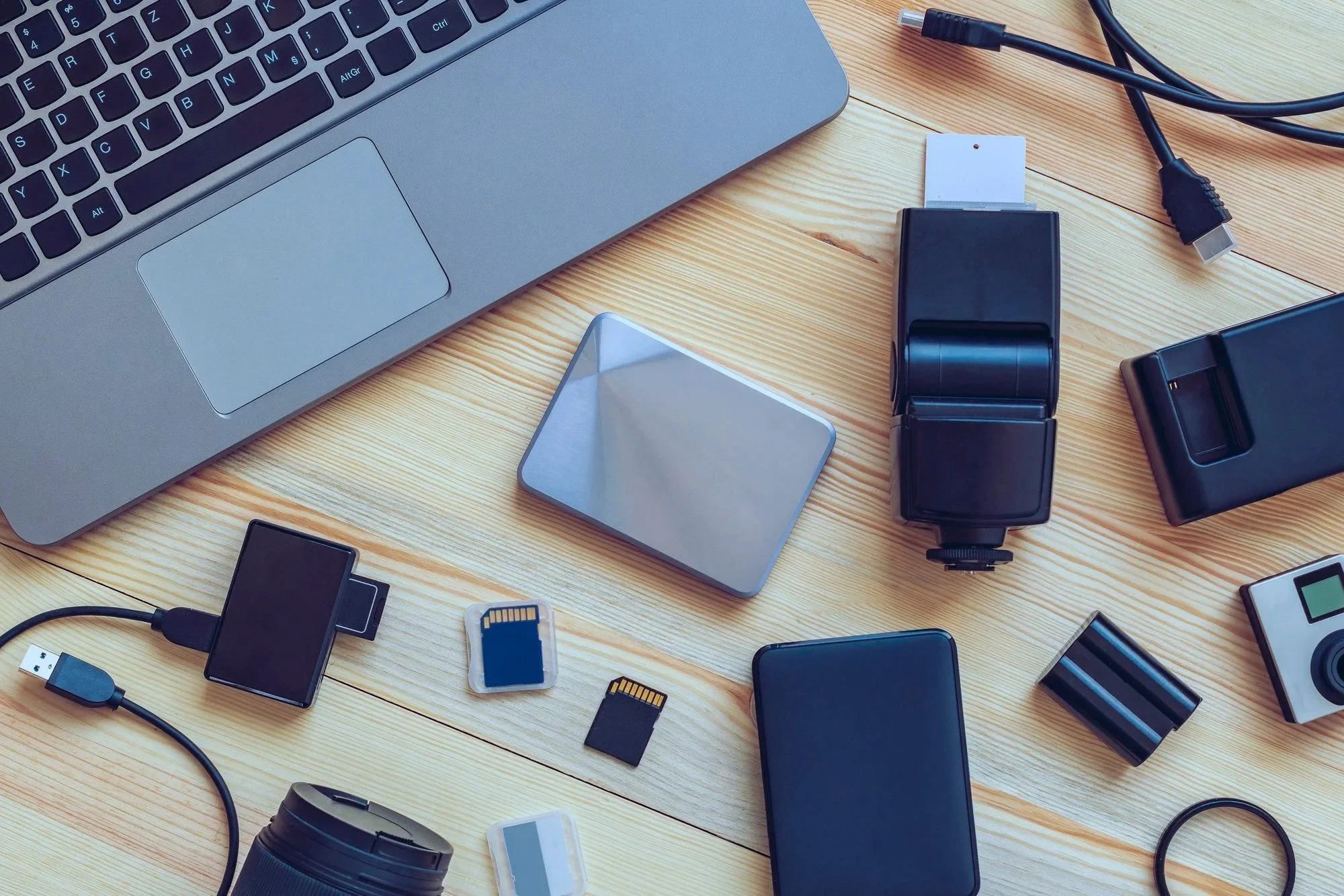 A laptop computer surrounded by external hard drives, phones, and SD cards