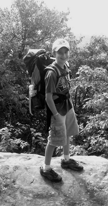 a photo of a boy wearing a hiking backpack standing on a mountaintop