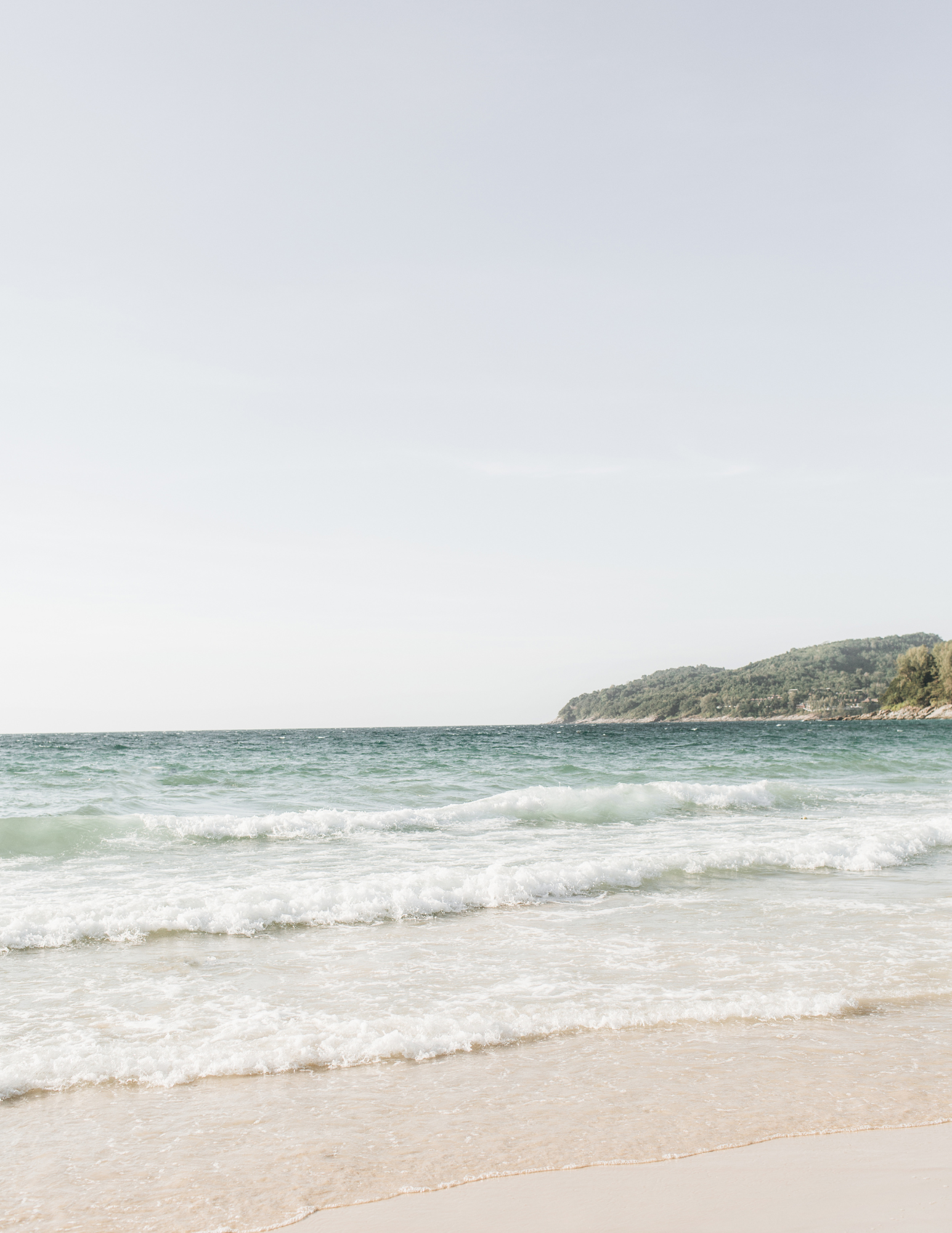 Beach view with soft waves and tree-covered hill in Los Cabos