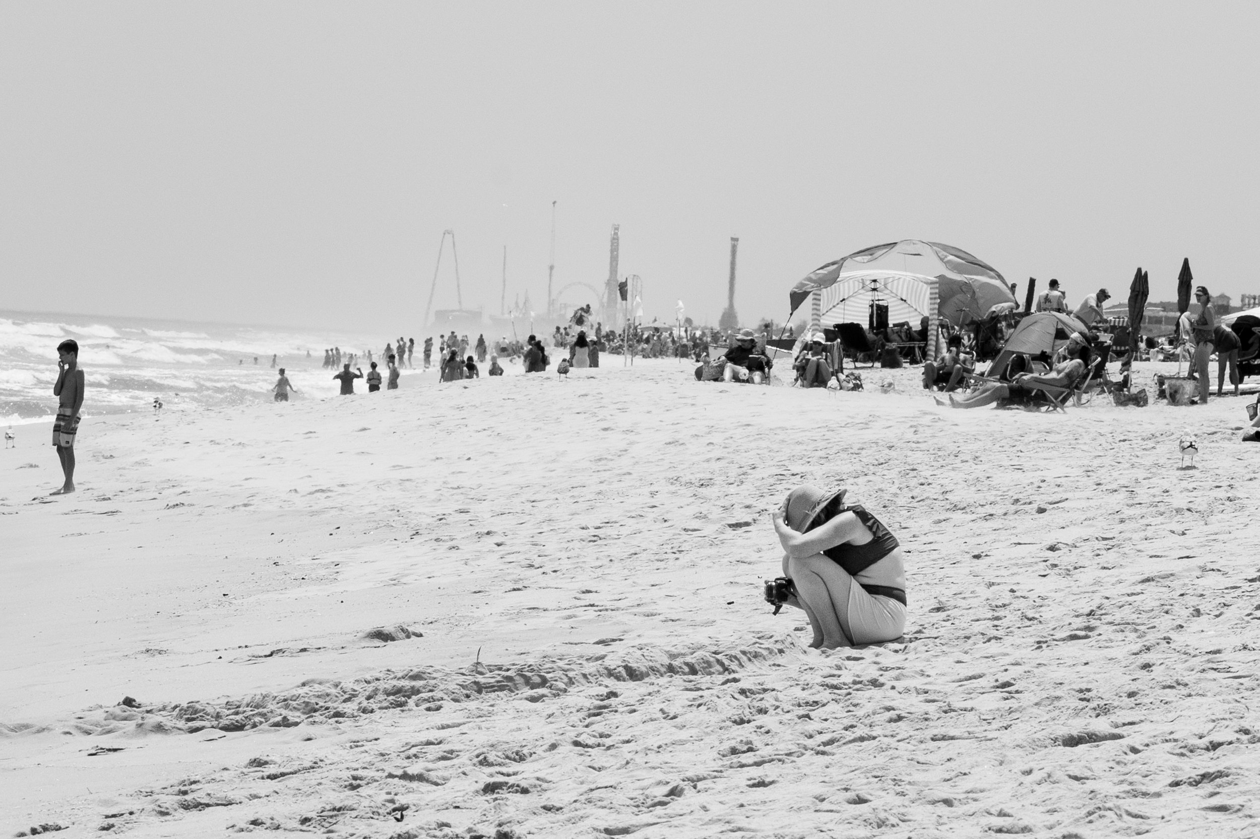 Documentary family photographer Kristi Tamcsin crouches to look at camera back on sunny beach
