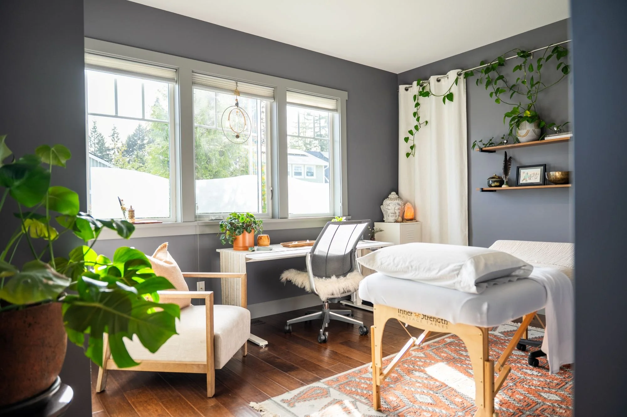 A peaceful healing room bathed in natural sunlight, filled with plants, crystals, soft surfaces, and a welcoming treatment table.