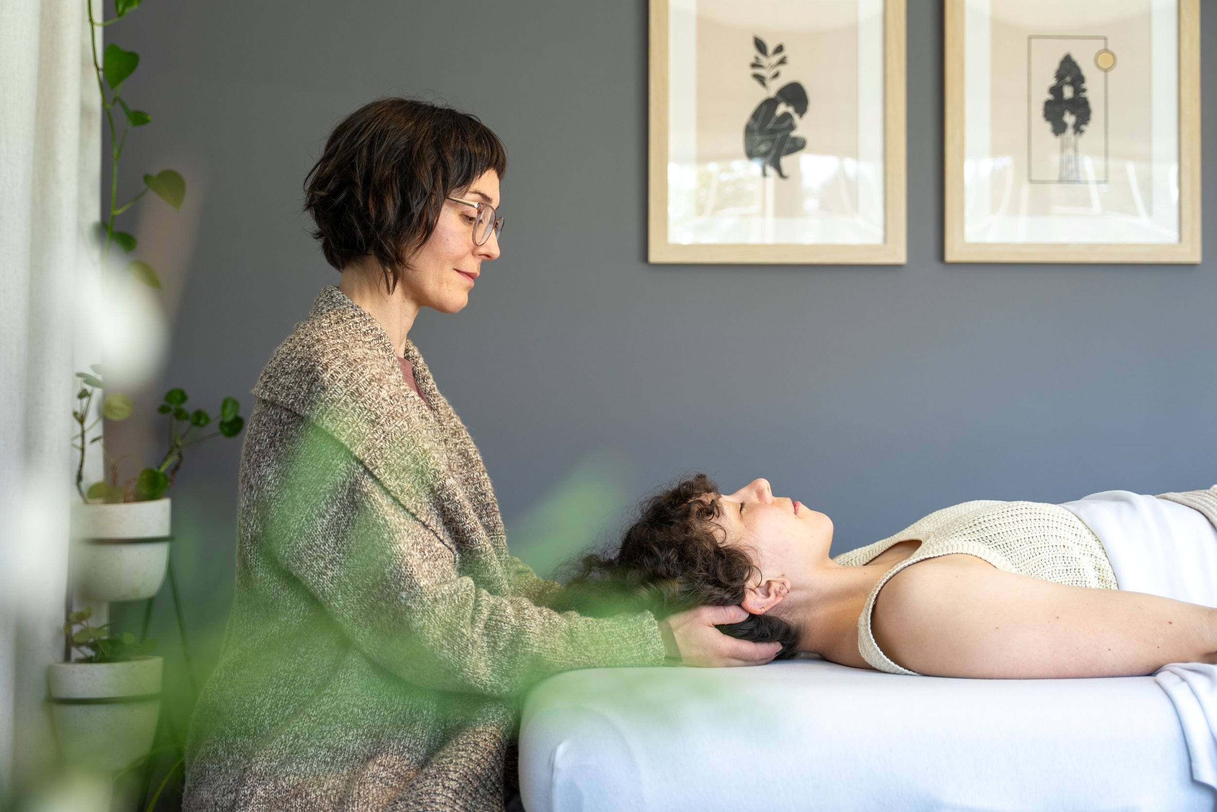 A side view of Leigh Blackburn offering intuitive energy healing or craniosacral therapy by gently cradling her client's head as they rest on the treatment table.