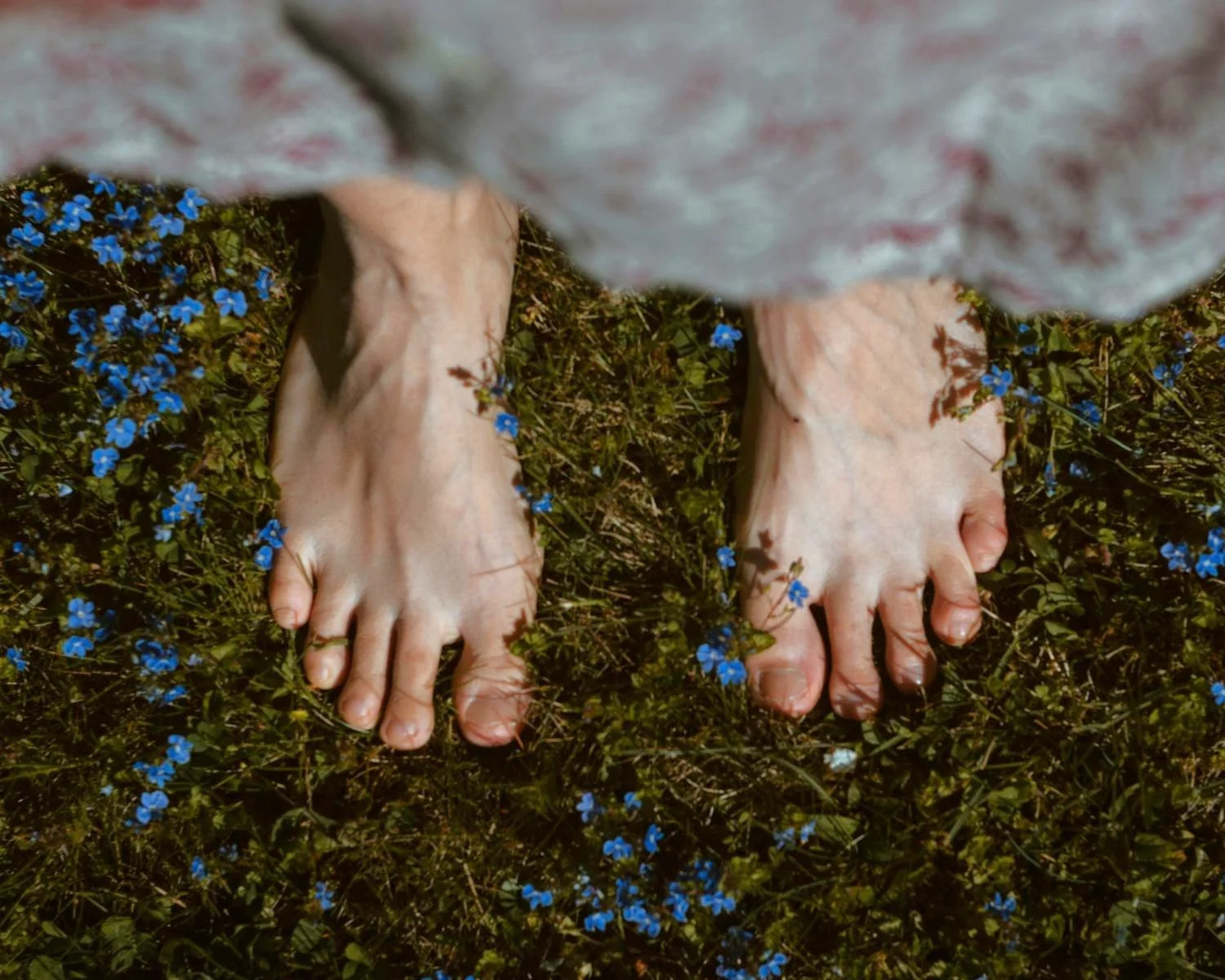 Woman with bare feet on grass filled with small purple blossoms.