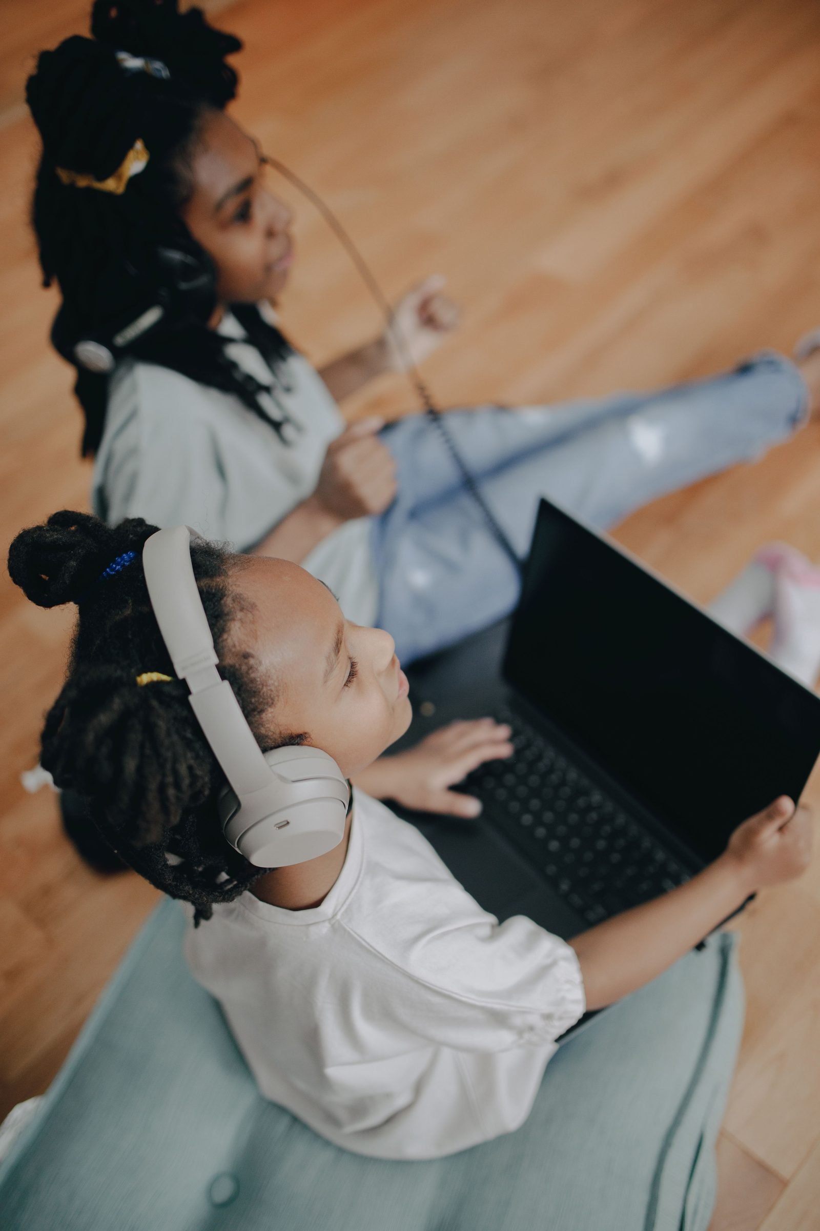 Two girls with headphones using a laptop at home
