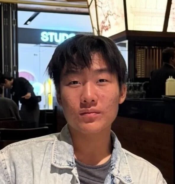 A young man in a denim jacket looking directly at the camera