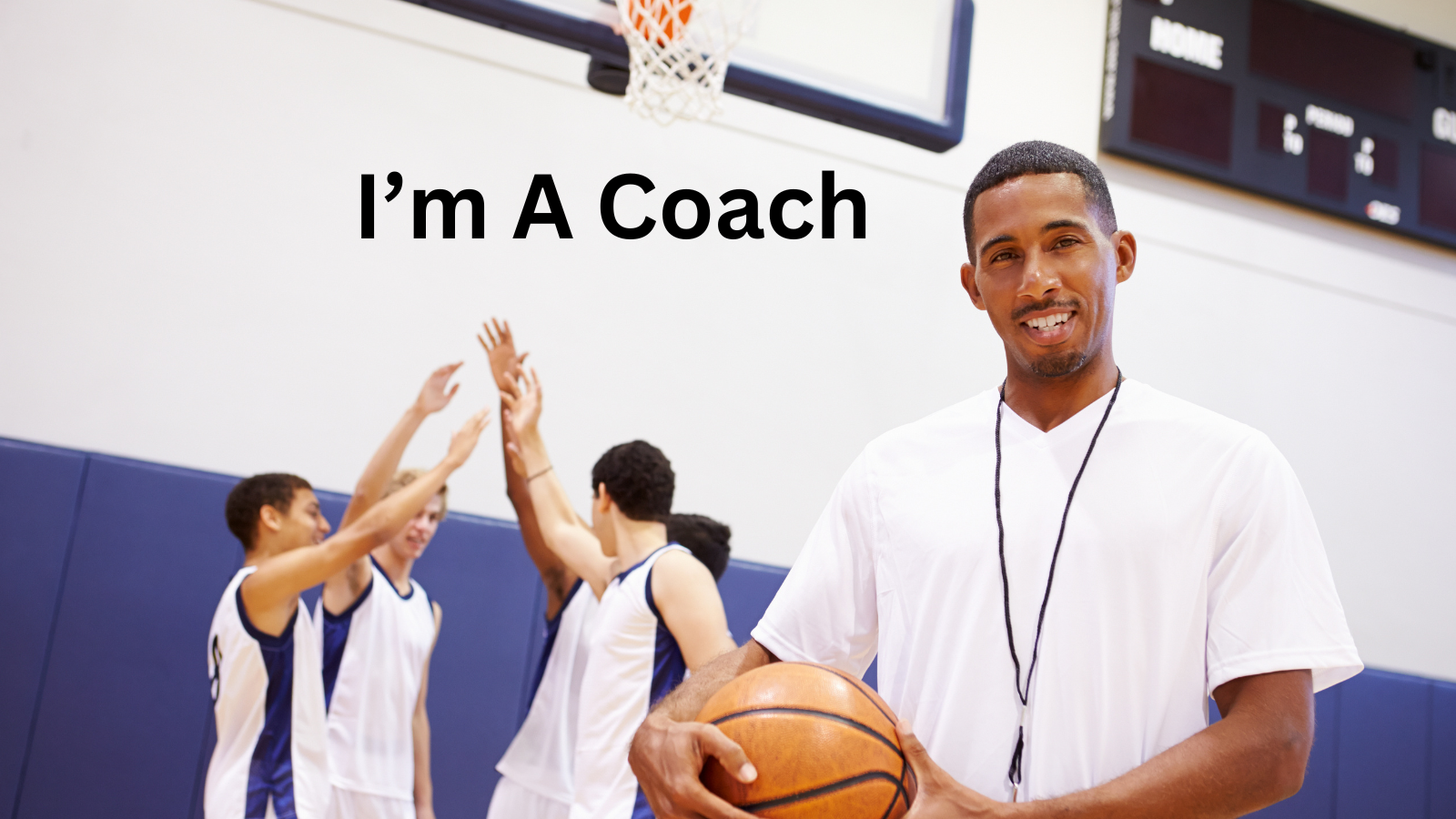 A coach standing in a basketball gym holding a basketball with a group of players in the background celebrating a game, with text overlay that says "I'm A Coach."
