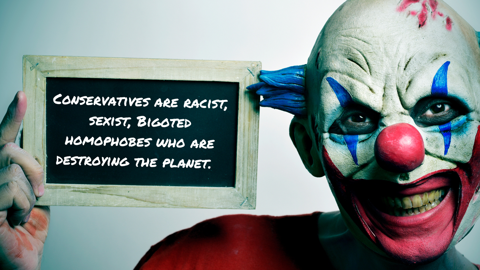 A person wearing a clown mask with blue hair, red nose, and bright makeup holding a chalkboard with a message about conservatives and homophobes.