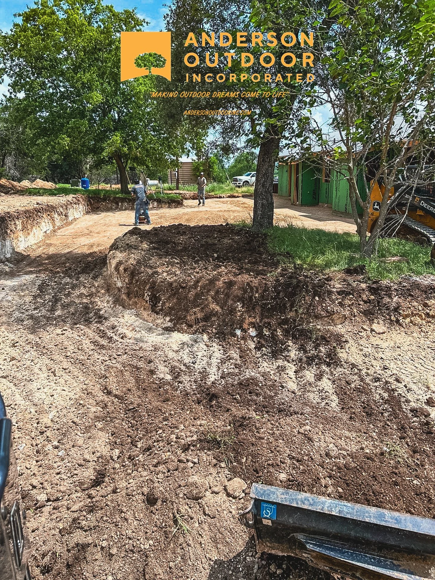 Excavation site with workers leveling the ground, surrounded by trees and construction equipment, for outdoor construction or landscaping project.
