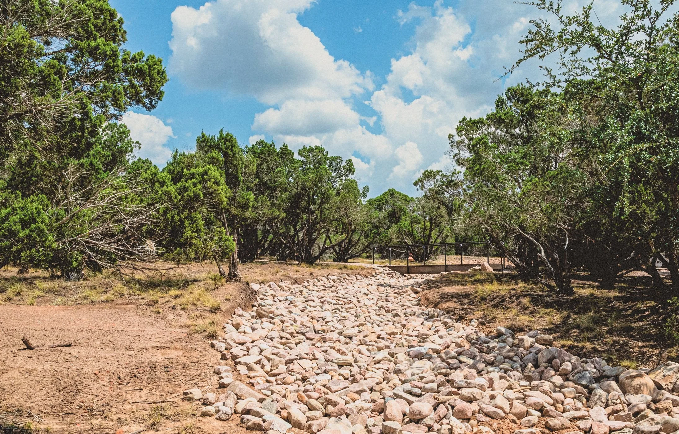 Finished river rock dry creek channel running through cedar and oak trees.