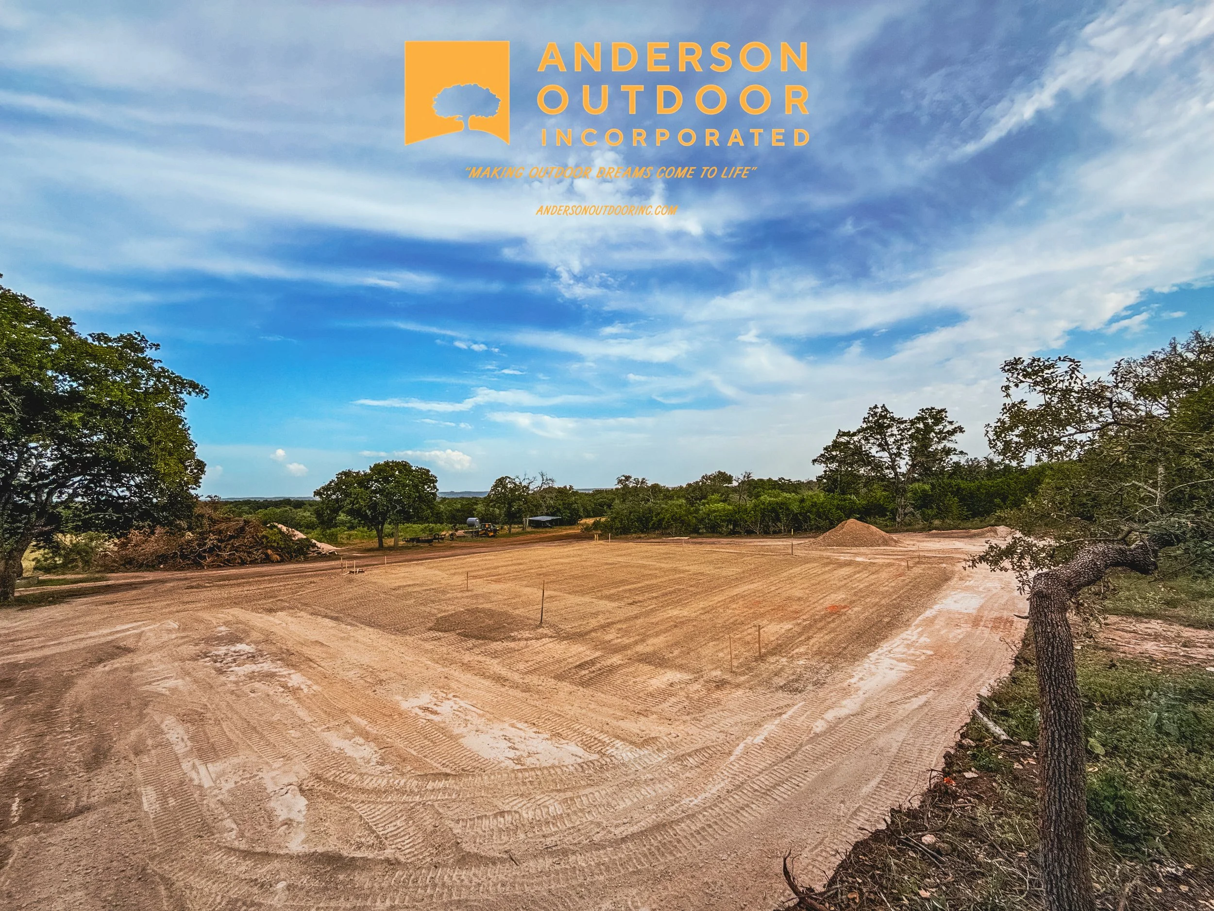 Construction site with cleared land, surrounding trees, blue sky with clouds, and a company logo for Anderson Outdoor Inc. in the upper part of the image.