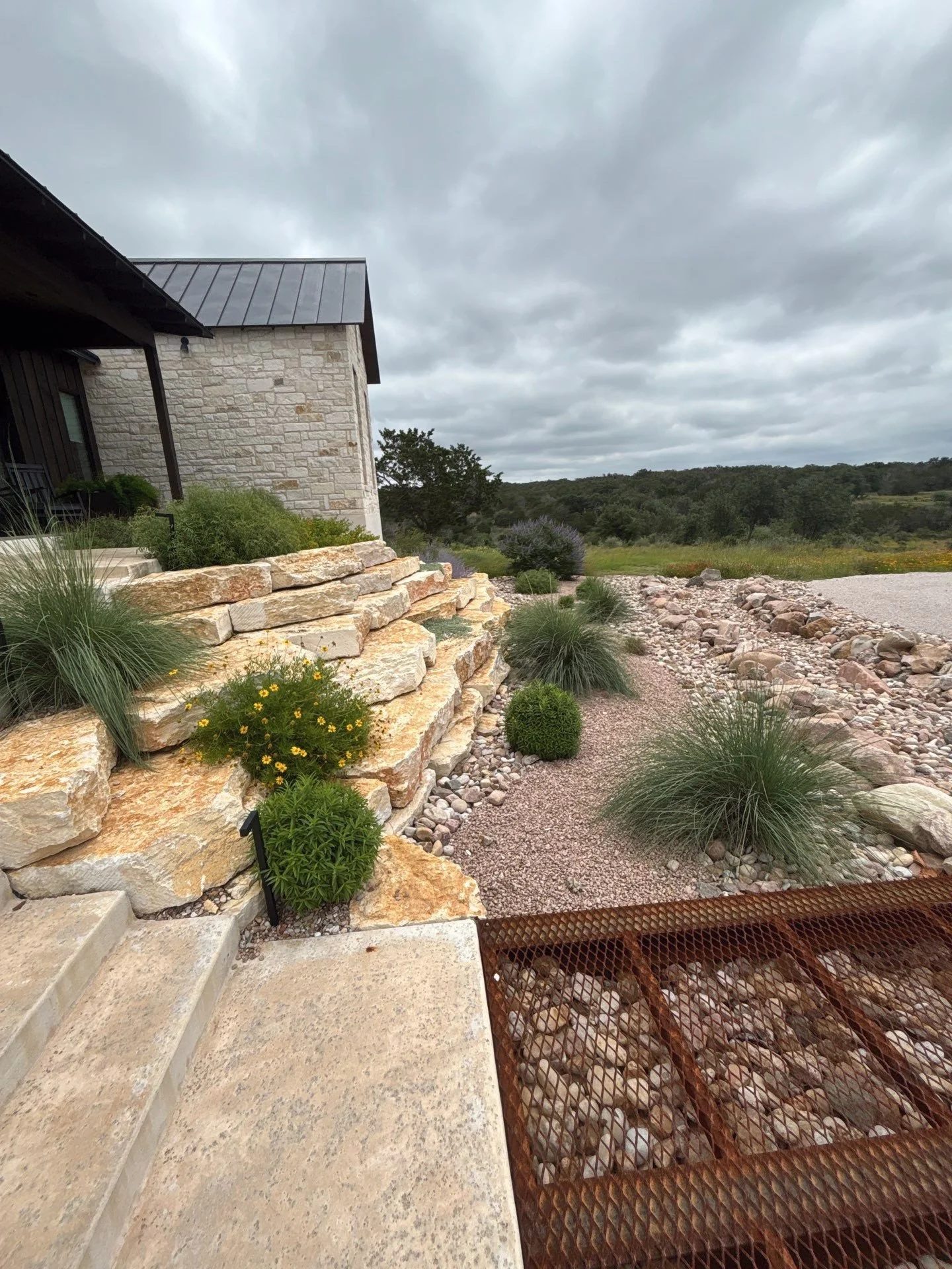 Limestone steps leading to a steel grate bridge over a river rock dry creek bed.