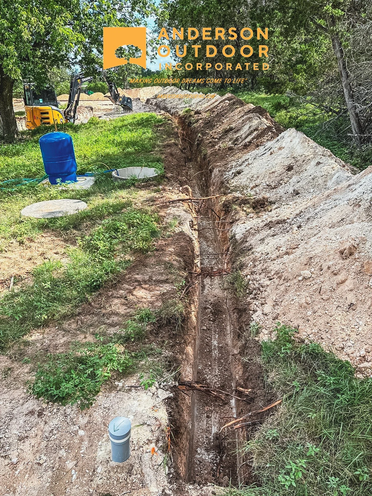 Construction site with an excavation trench and construction equipment, trees in the background, and logo overlay of Anderson Outdoor Incorporated.