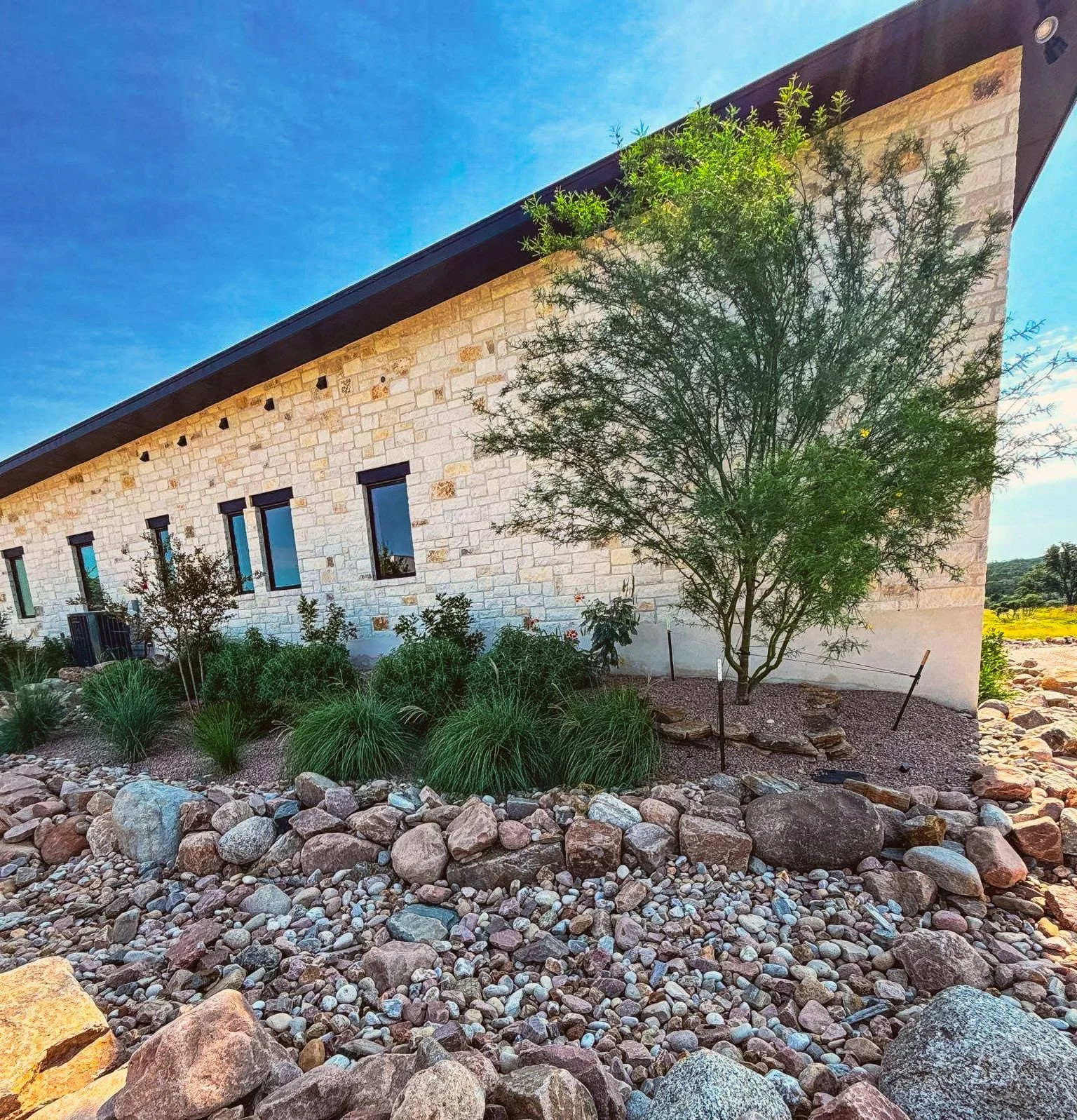 Rock-lined swale and native planting along a modern limestone home.