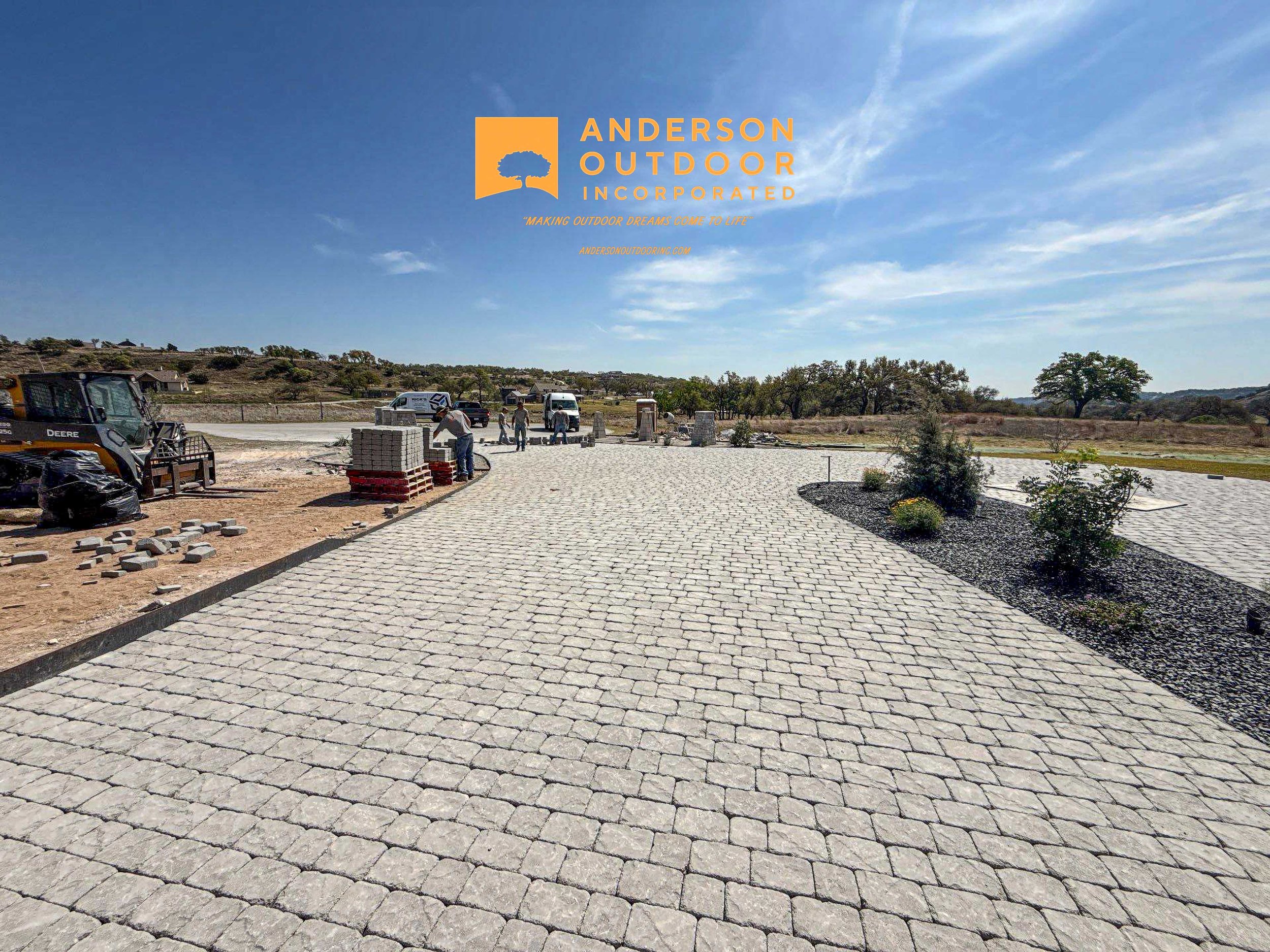 Construction site with paved pathway, small trees, construction workers, and equipment under a blue sky with some clouds.