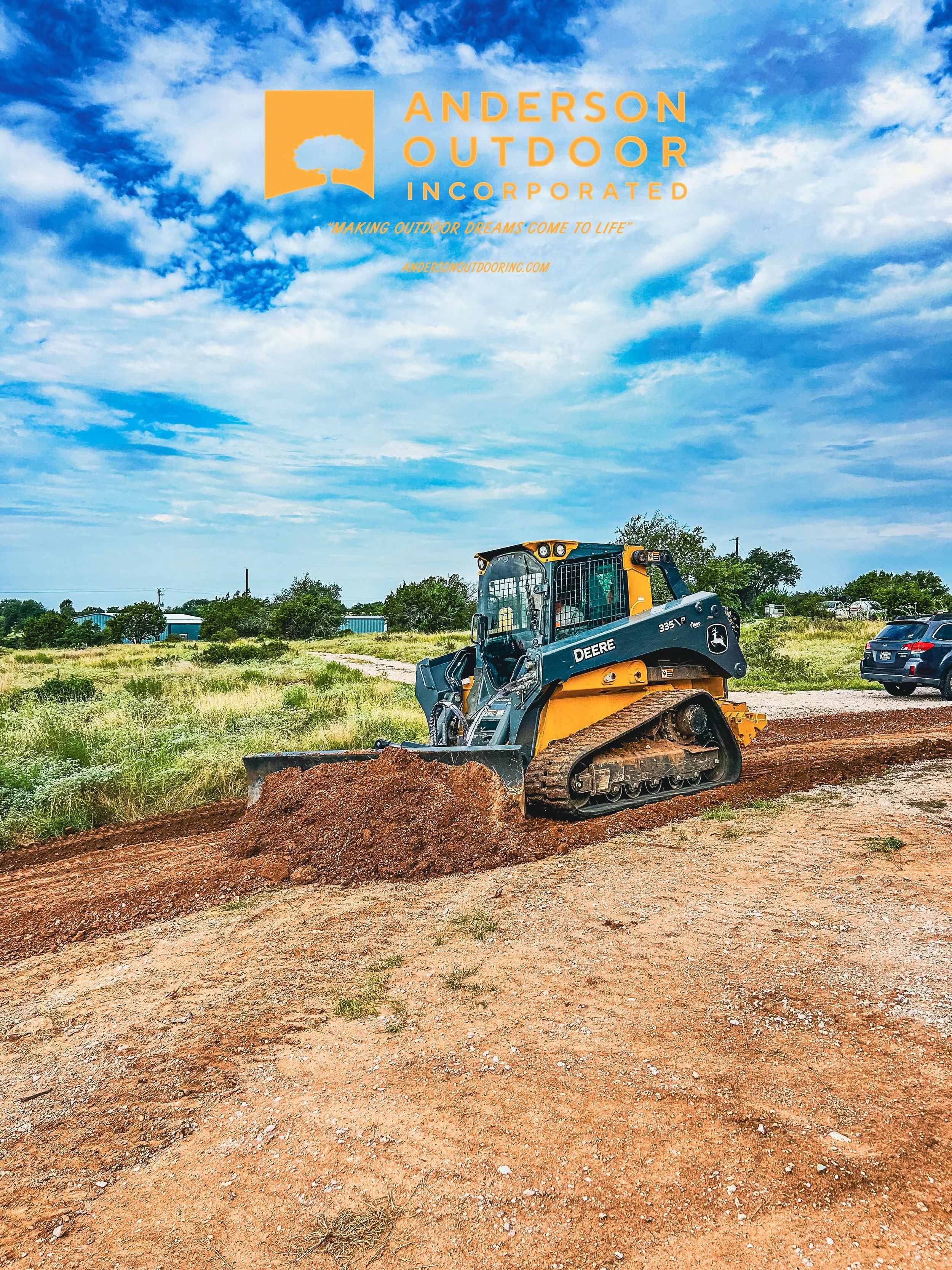 A John Deere bulldozer clearing a dirt path on a construction site with a blue sky and scattered clouds in the background.