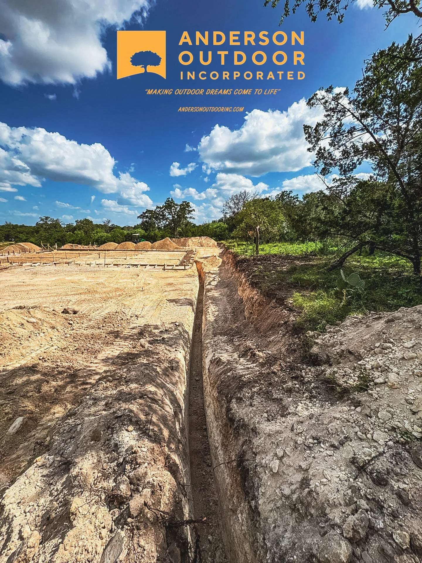 Photo of a construction site with a deep trench in the foreground, dirt mounds in the background, trees on the right side, and a blue sky with clouds. The top left corner has a logo and text for Anderson Outdoor Incorporated.