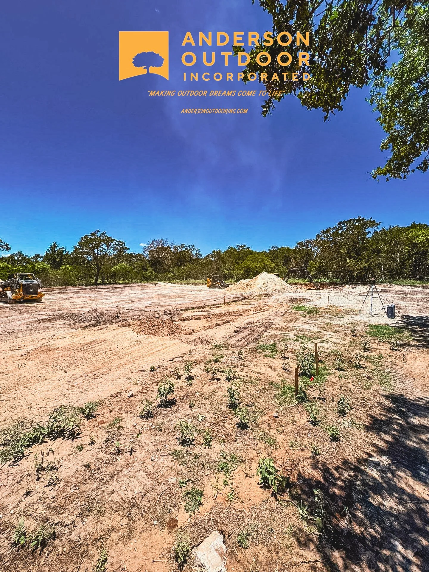 Construction site with dirt and small plants, trees in background, branding for Anderson Outdoor Incorporated in the upper left corner.