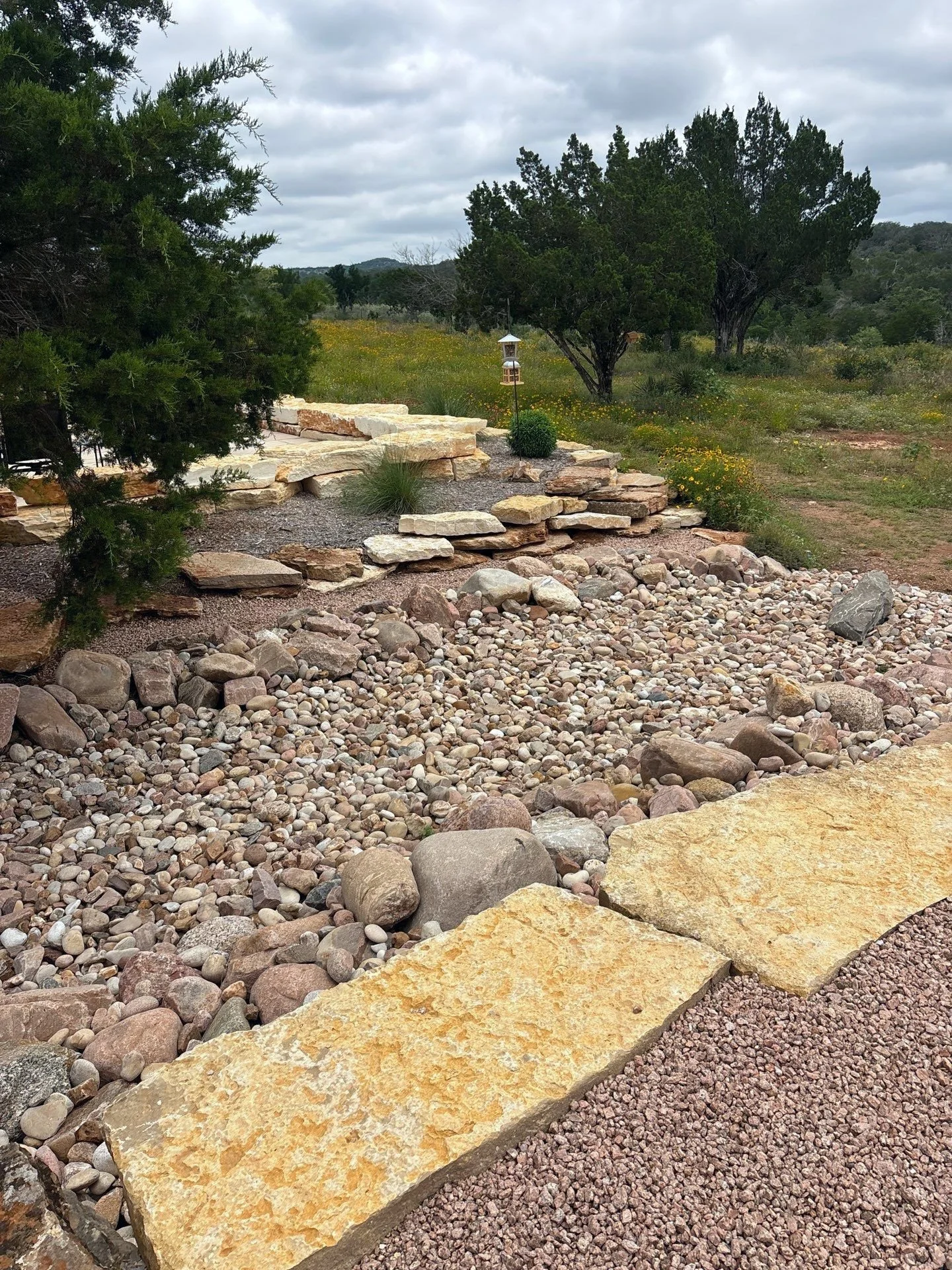 River rock dry creek channel with limestone steppers and native plants.