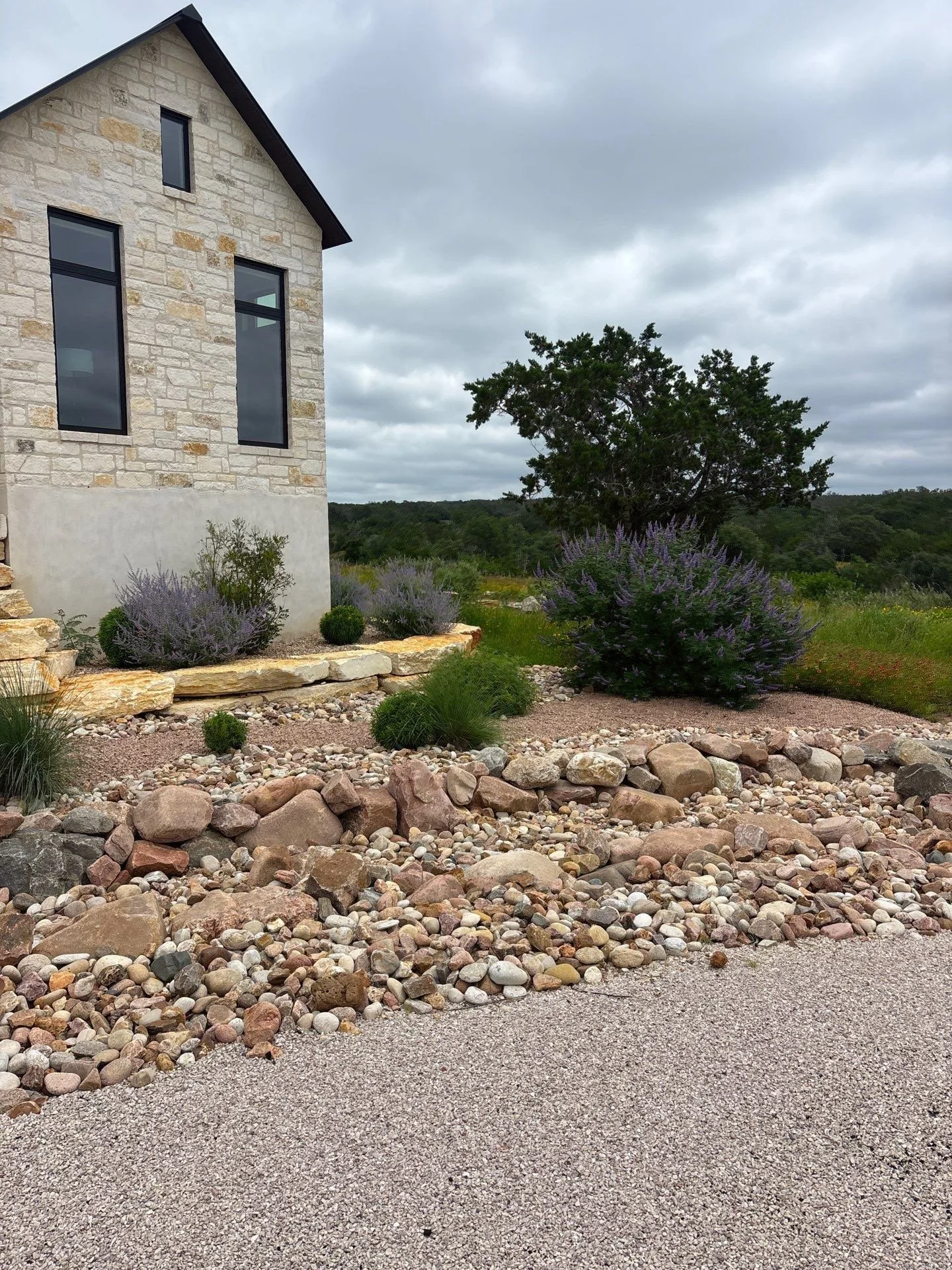 River rock dry creek bed along a limestone home with salvia and native grasses.