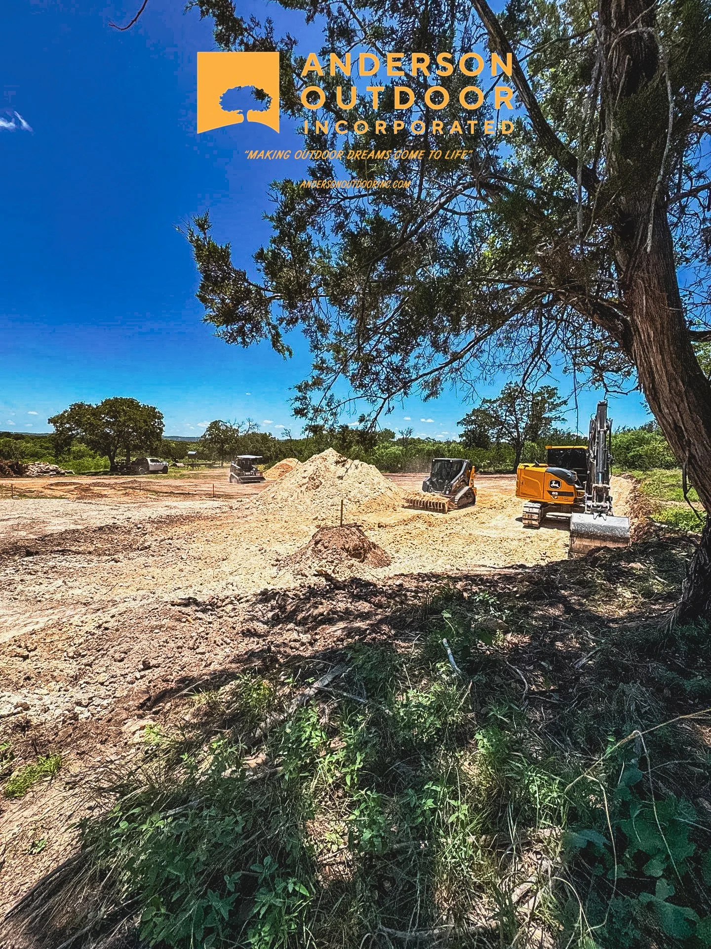 Construction site with excavators, piles of dirt, and trees, under a clear blue sky, featuring the Anderson Outdoor Incorporated logo and company slogan.