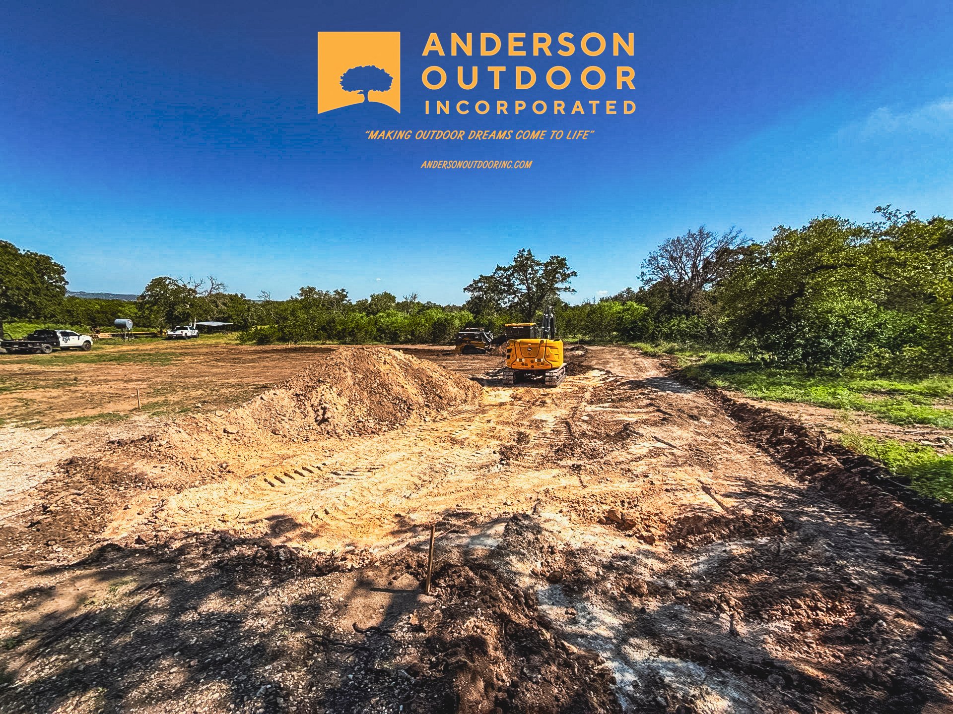 Construction site with dirt, heavy machinery, and green trees under a clear blue sky. Logo of Anderson Outdoor Inc. at the top left.