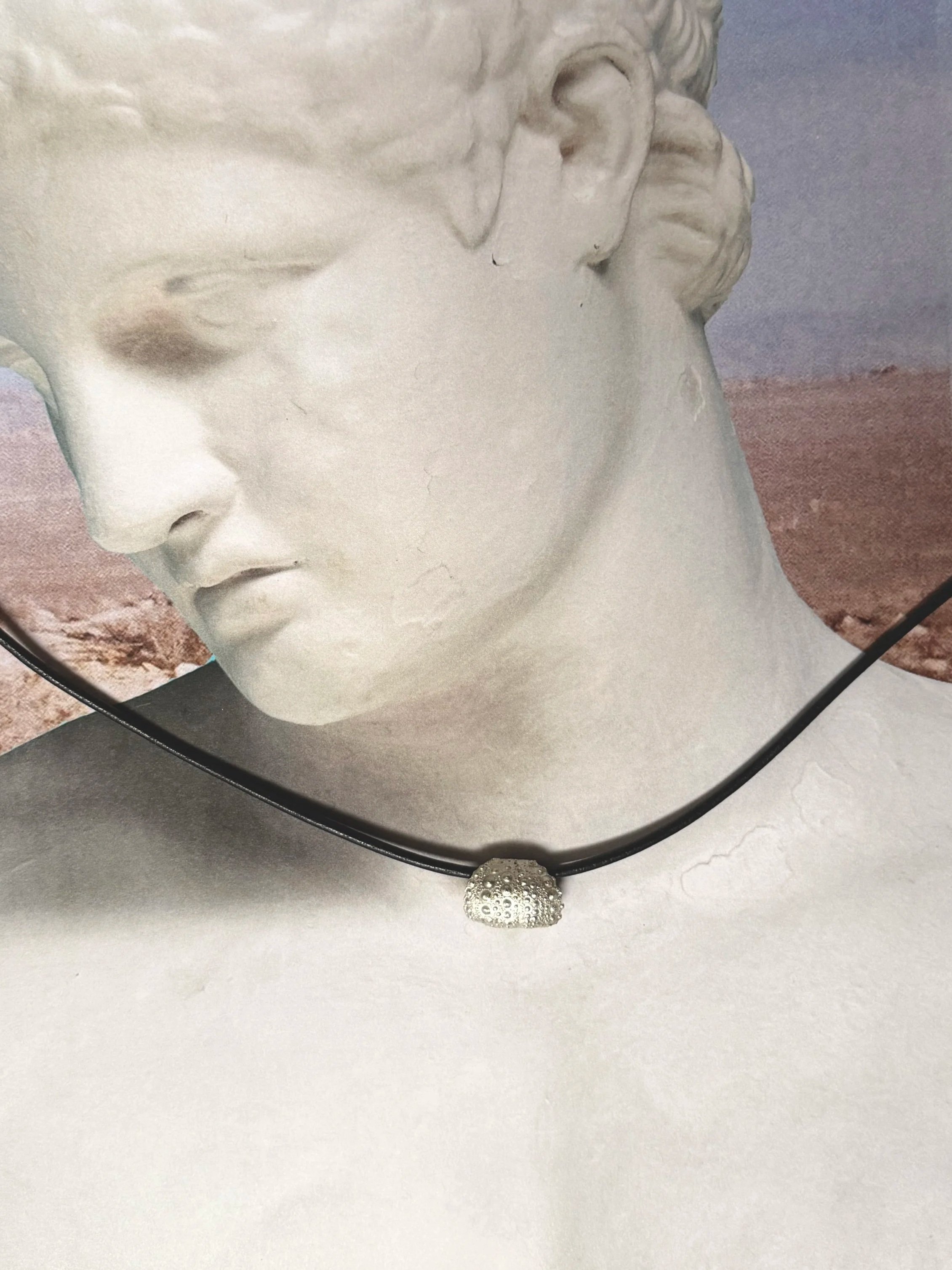 Sterling silver sea urchin pendant on leather cord, displayed on classical bust