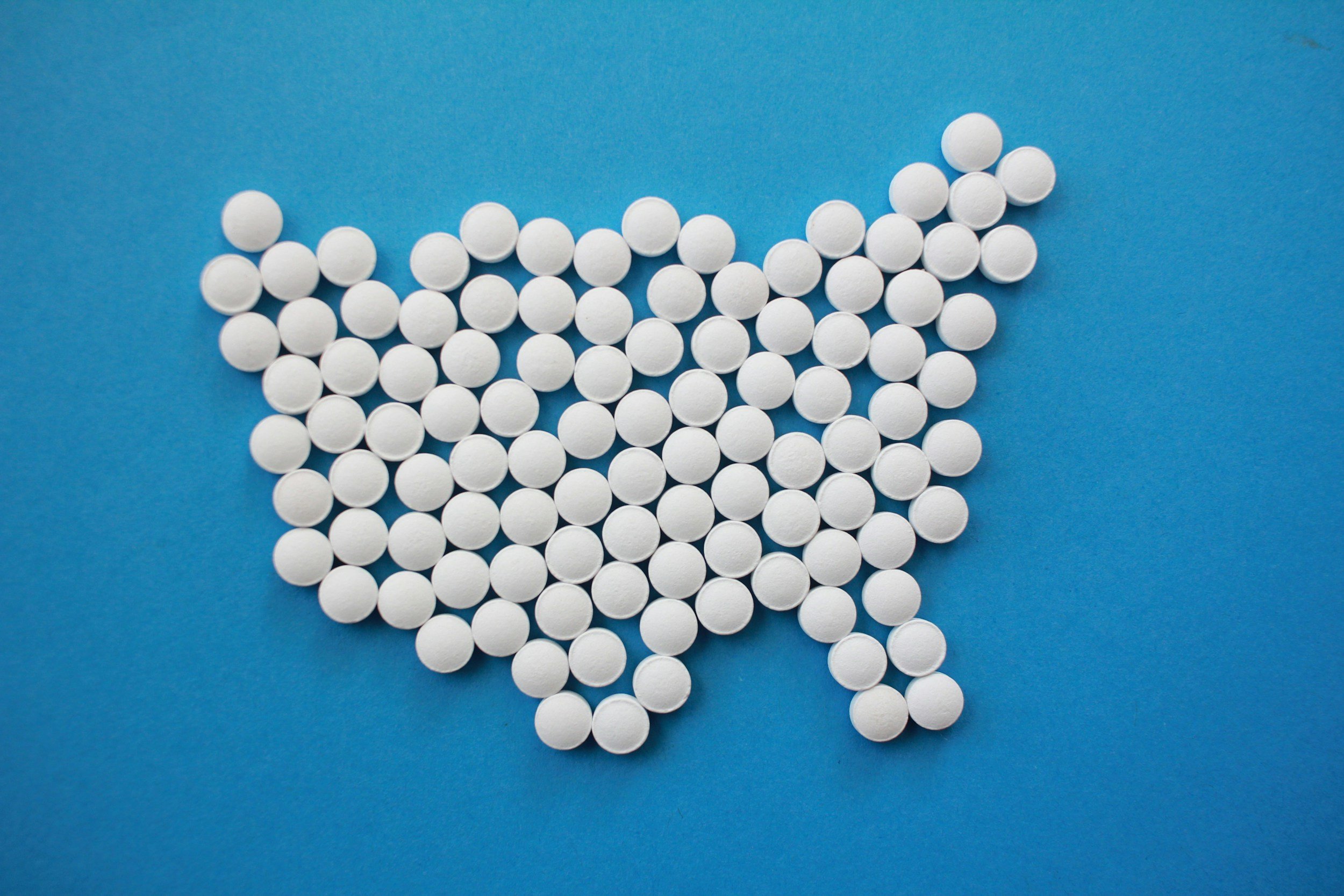White round pills arranged in the shape of the United States on a blue background.