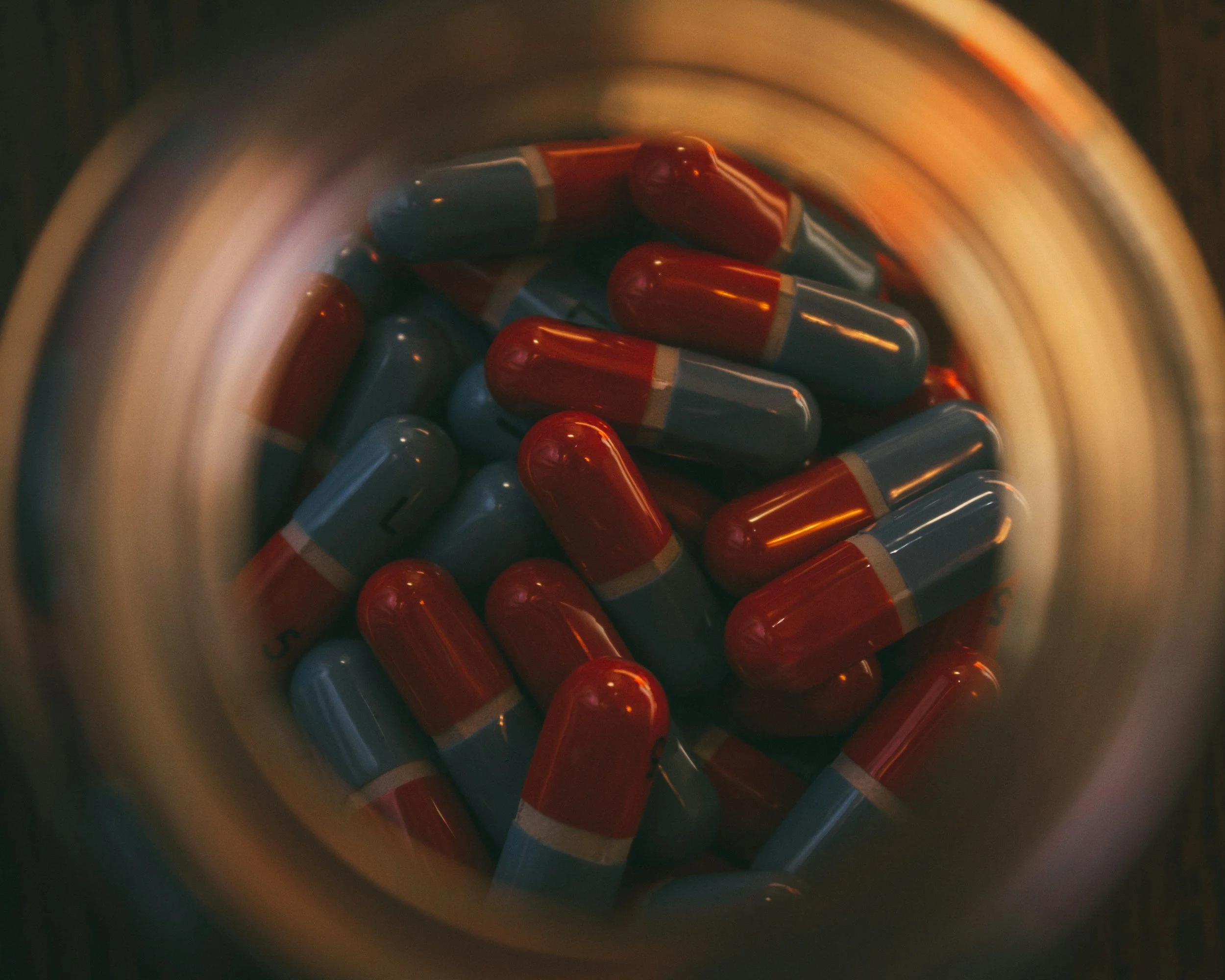 Close-up view of red and blue capsules inside a medicine bottle, seen from above.
