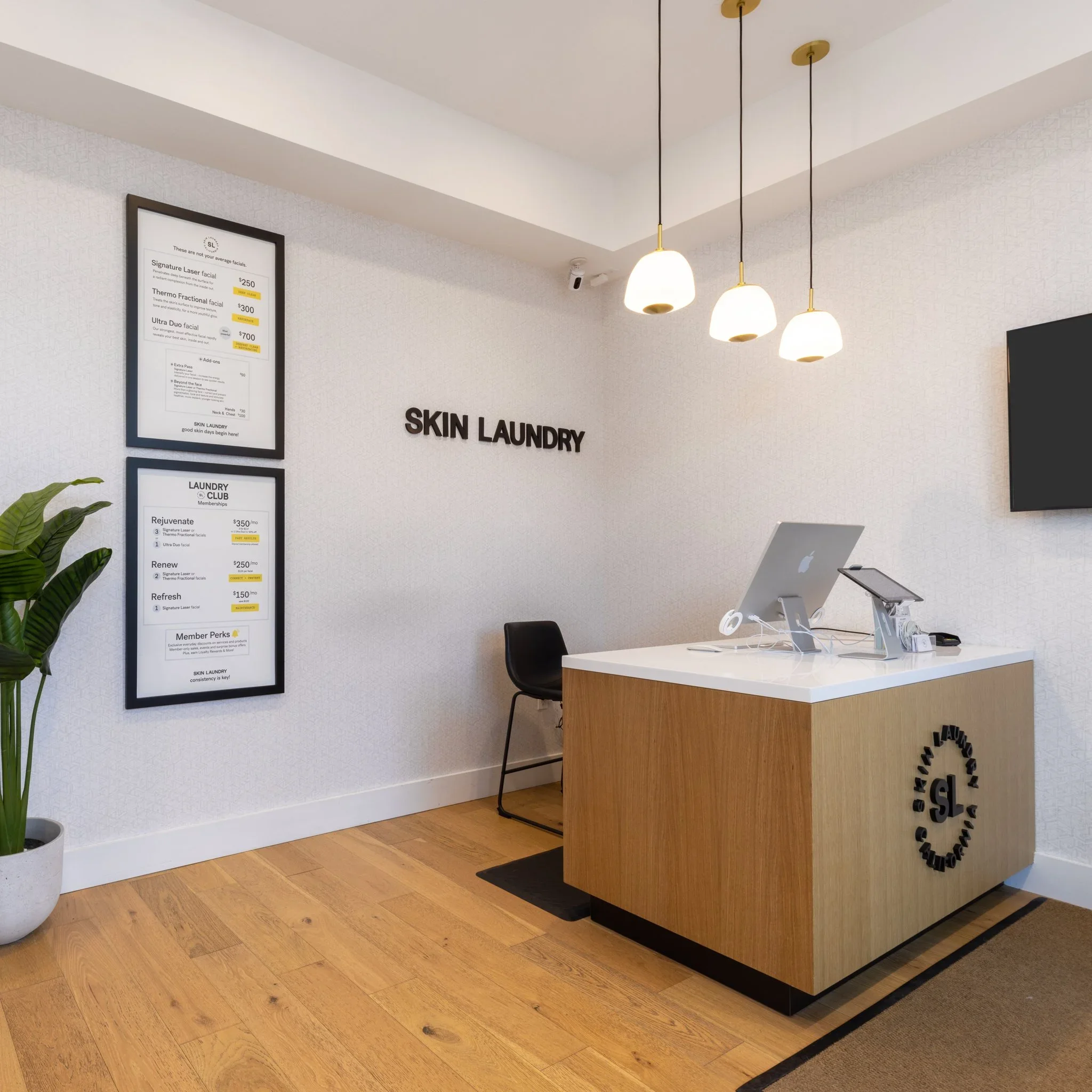 Interior of a skin laundry clinic featuring a reception desk, wall art with menu prices, and modern lighting fixtures hanging from the ceiling.