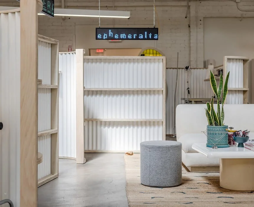 Modern office space with white furniture, plants, and shelving, illuminated by overhead lighting, featuring a digital sign with the word 'Schnebergeralta'.