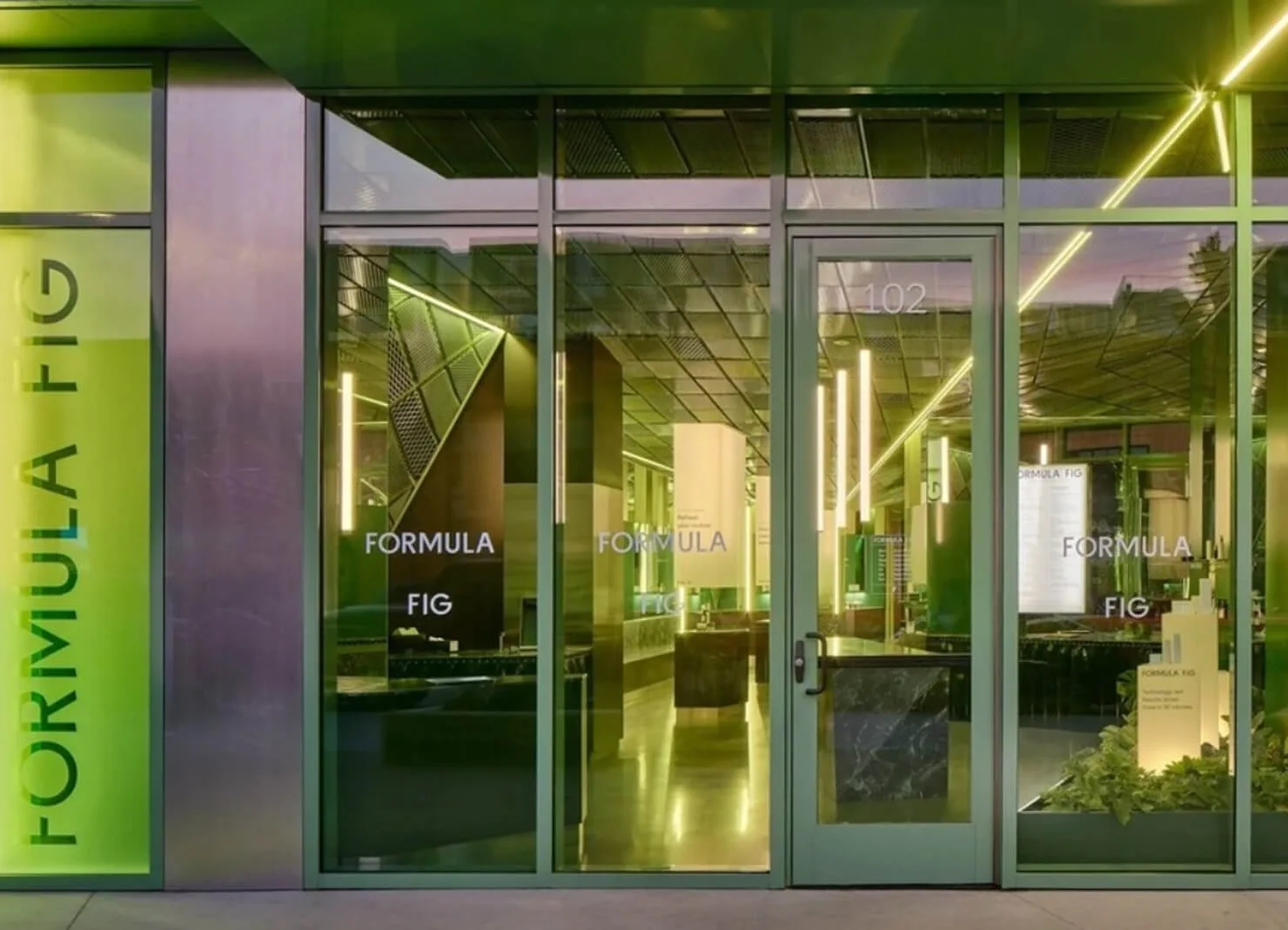 Modern storefront with glass doors and windows, displaying the words 'formula' and 'fig' multiple times, with a green vertical sign on the left reading 'FOURIUM AFLG', and interior with sleek design and bright lighting.