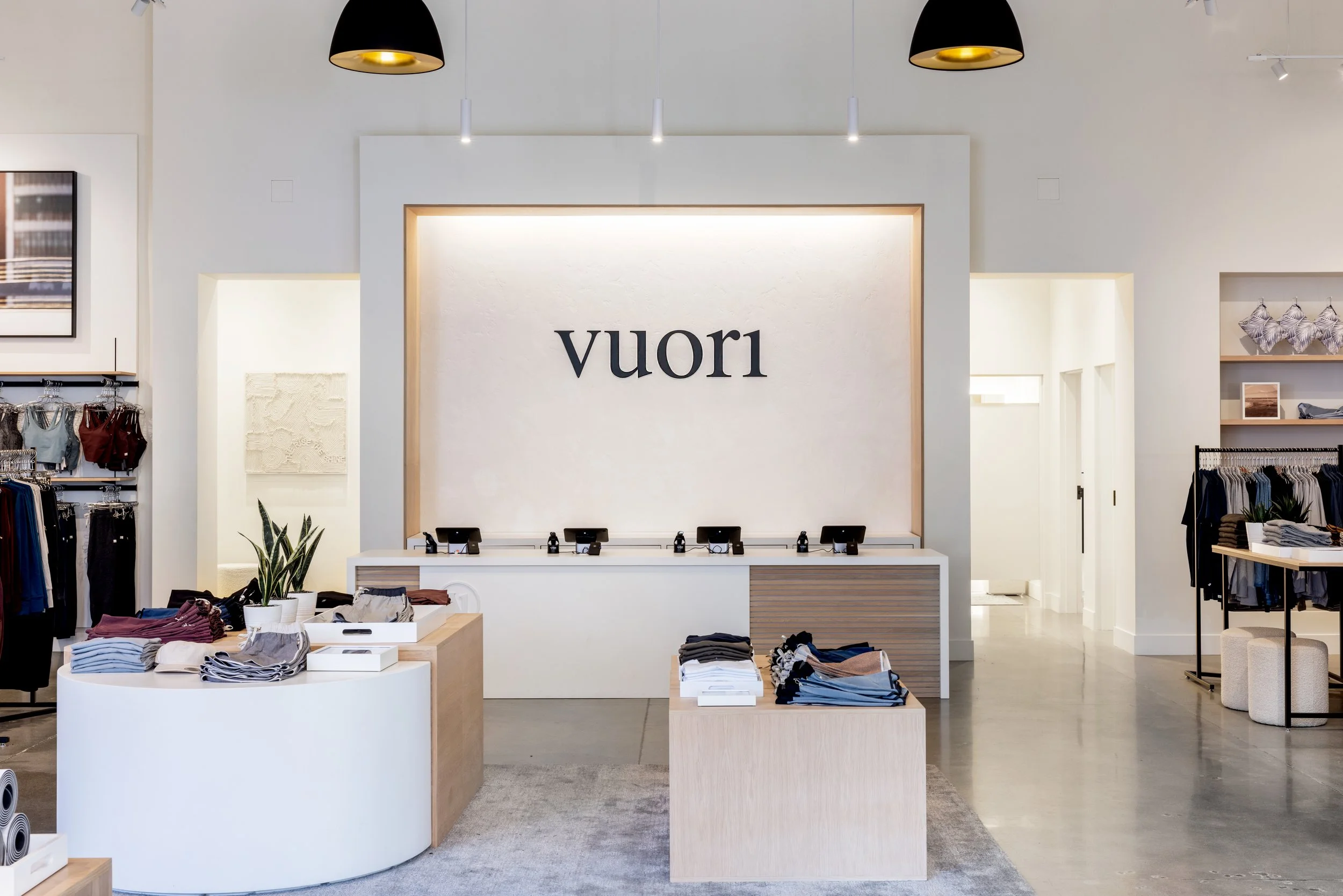 Interior of a clothing store with displays of folded clothes, racks of garments, and a large sign that reads 'vuori' on the back wall.