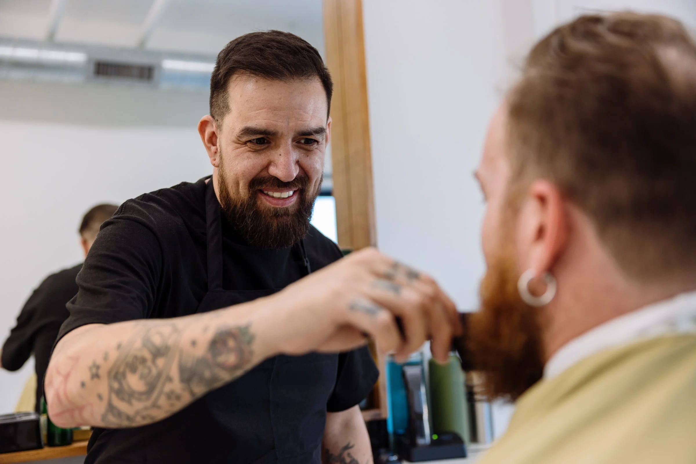 Friendly Austin barber smiling while trimming a client’s beard at Honest Barber barbershop.