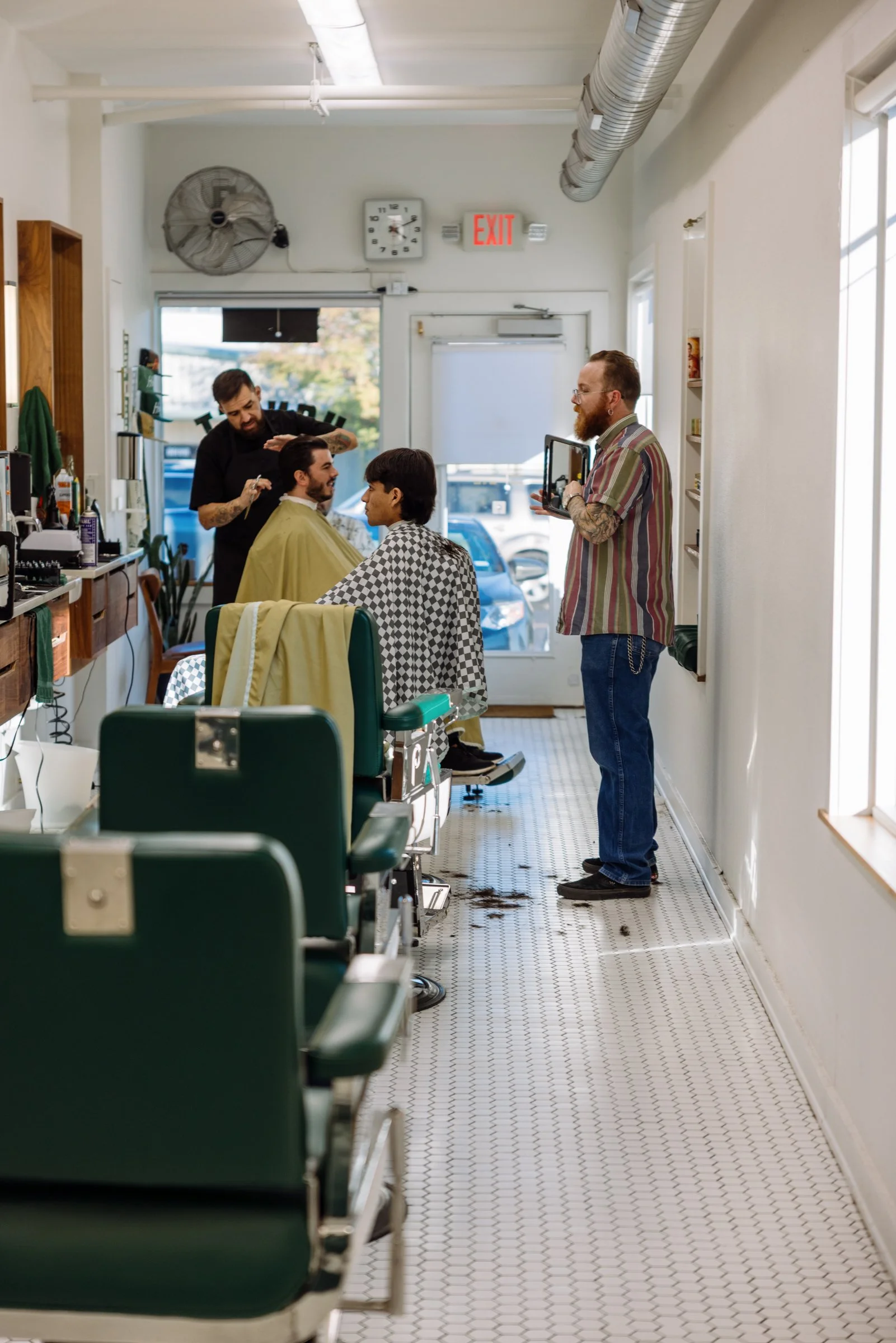 Wide interior view of Honest Barber in Austin Texas showing barbers cutting hair in a clean, modern men’s barbershop.