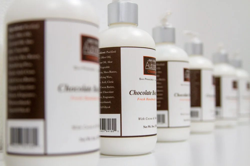 Multiple bottles of luxurious chocolate body lotion lined up on a shelf, labeled 'Chocolate Body' with a pump dispenser.