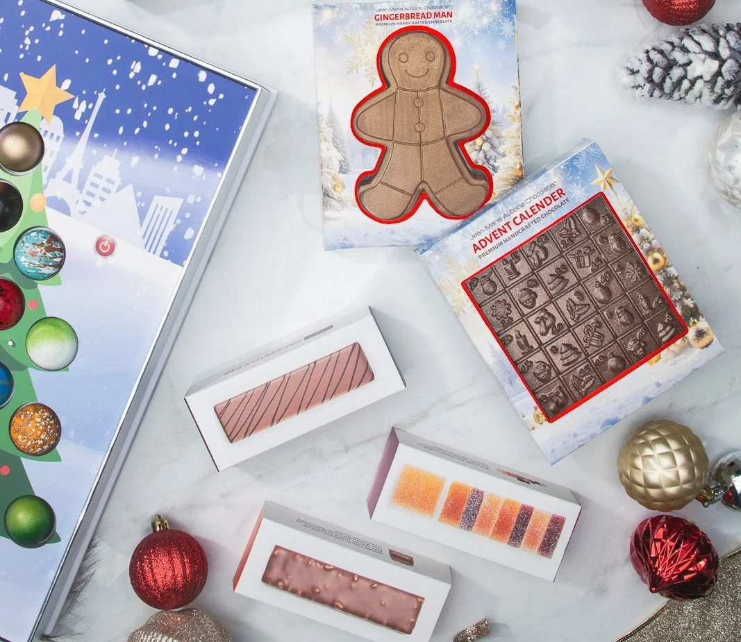 Luxury holiday chocolate collection featuring a gingerbread man figurine, advent calendar, artisan chocolate bars, and gourmet fruit jellies styled with festive décor.