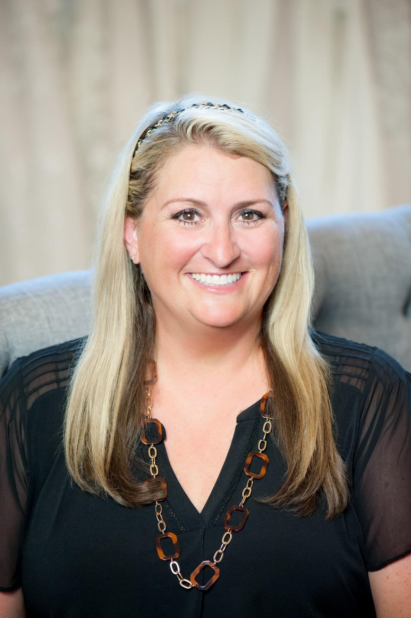 Smiling woman with blonde hair wearing a black top and necklace