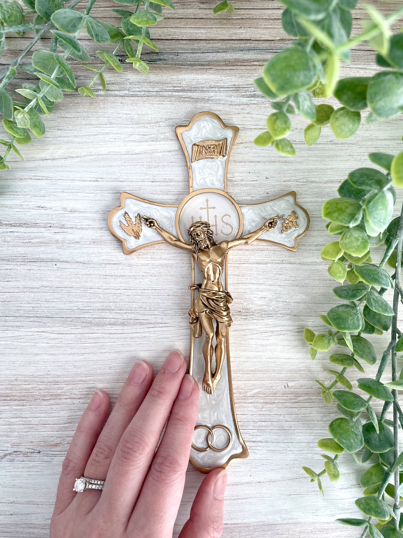 An ornate white epoxy crucifix with gold borders and a gold corpus. A hand is shown for scale.