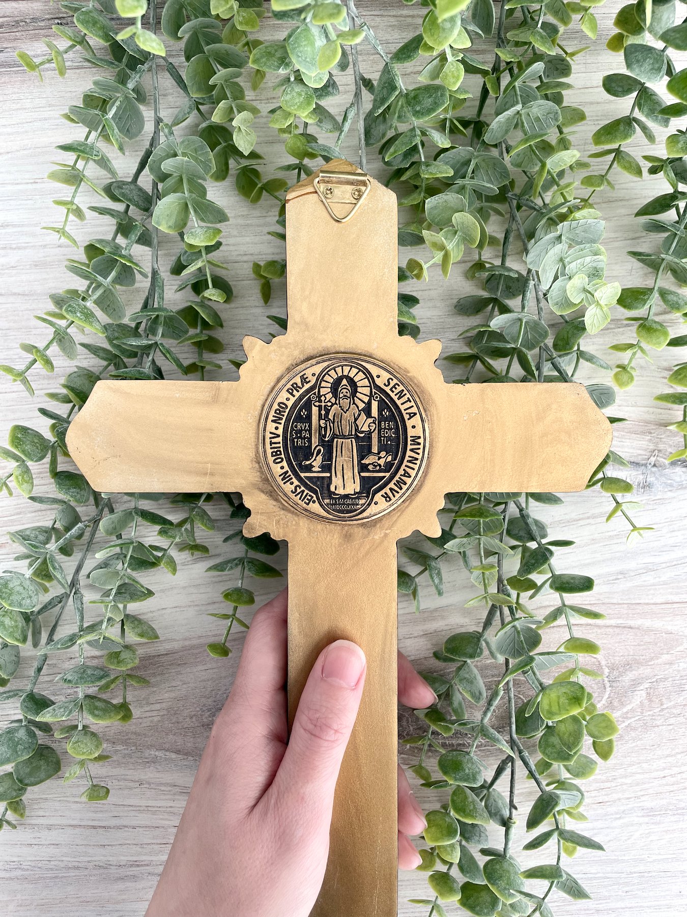 The back of a bronze-colored resin crucifix with a Benedict cross symbol.