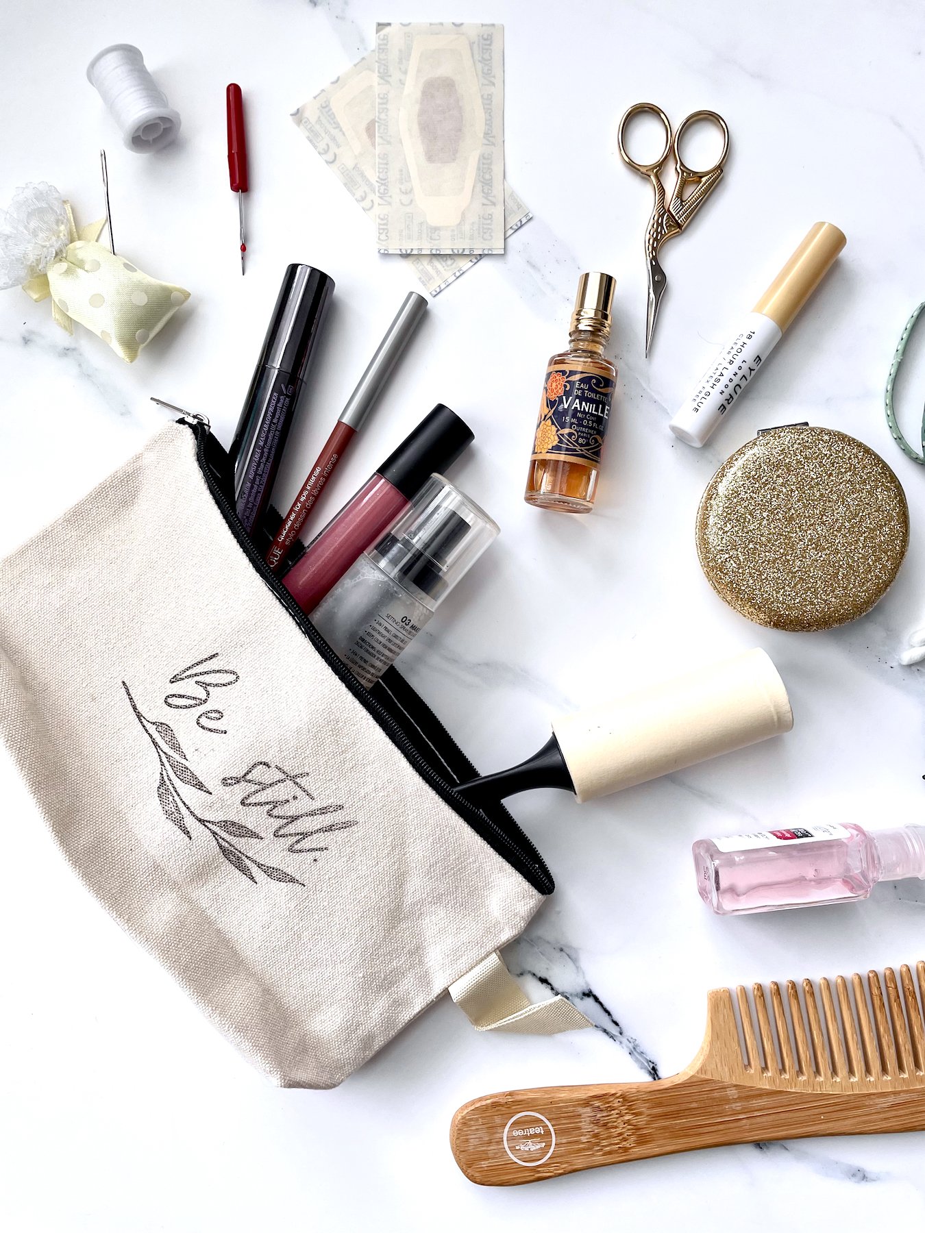 Canvas pouch stamped with cursive text "Be still." Pouch shows everything you need for your wedding day "emergency kit," including makeup, small scissors, bandaids, a lint roller, and much more!