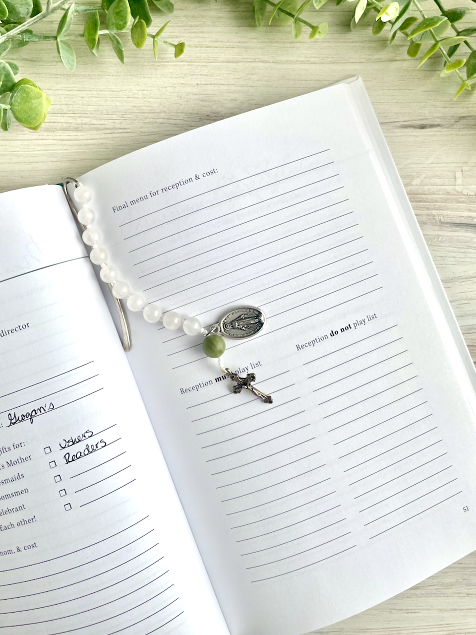 Gemstone bookmark with a decade's worth of rosary beads, miraculous medal, and small crucifix, resting on the Covenant Wedding Planner.