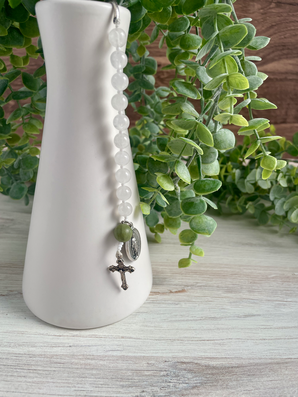 Gemstone bookmark with a decade's worth of rosary beads, miraculous medal, and small crucifix, hanging from a vase. Green Our Father bead.