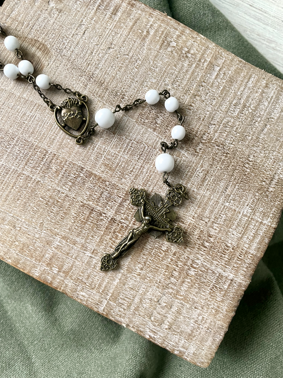 Smooth white beaded rosary with bronze chain links. Bronze sunburst crucifix and bronze Sacred Heart centerpiece.
