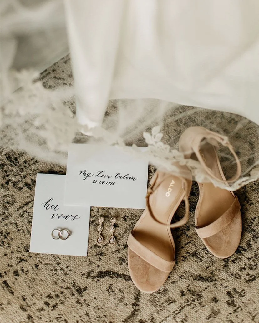 Wedding shoes, earrings, wedding rings, and a note with the date 10-24-2020 and the words "My Love Constant" on a textured rug.