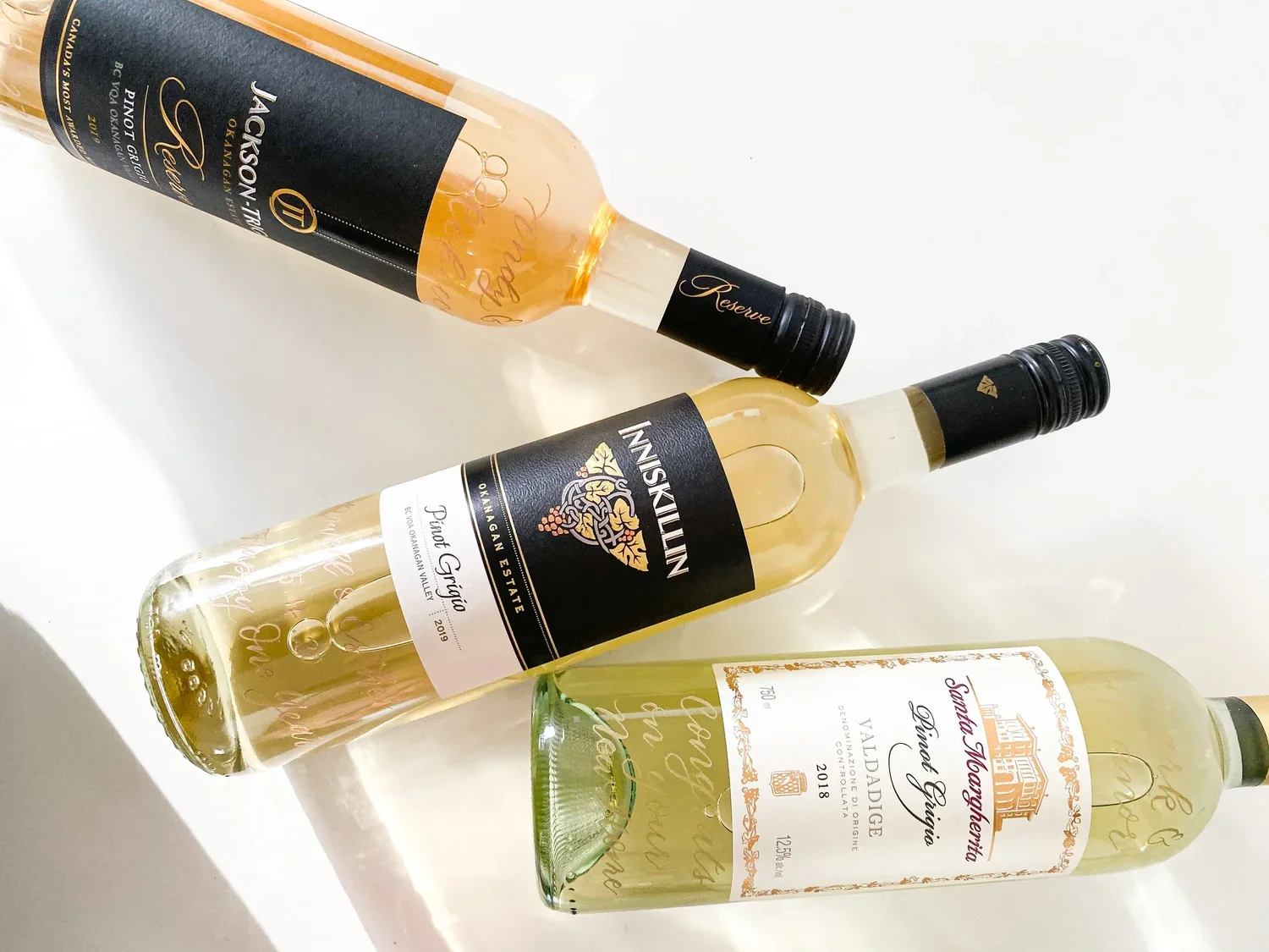 Three bottles of white wine lying on a white surface in a diagonal arrangement. The bottles are from different wineries.