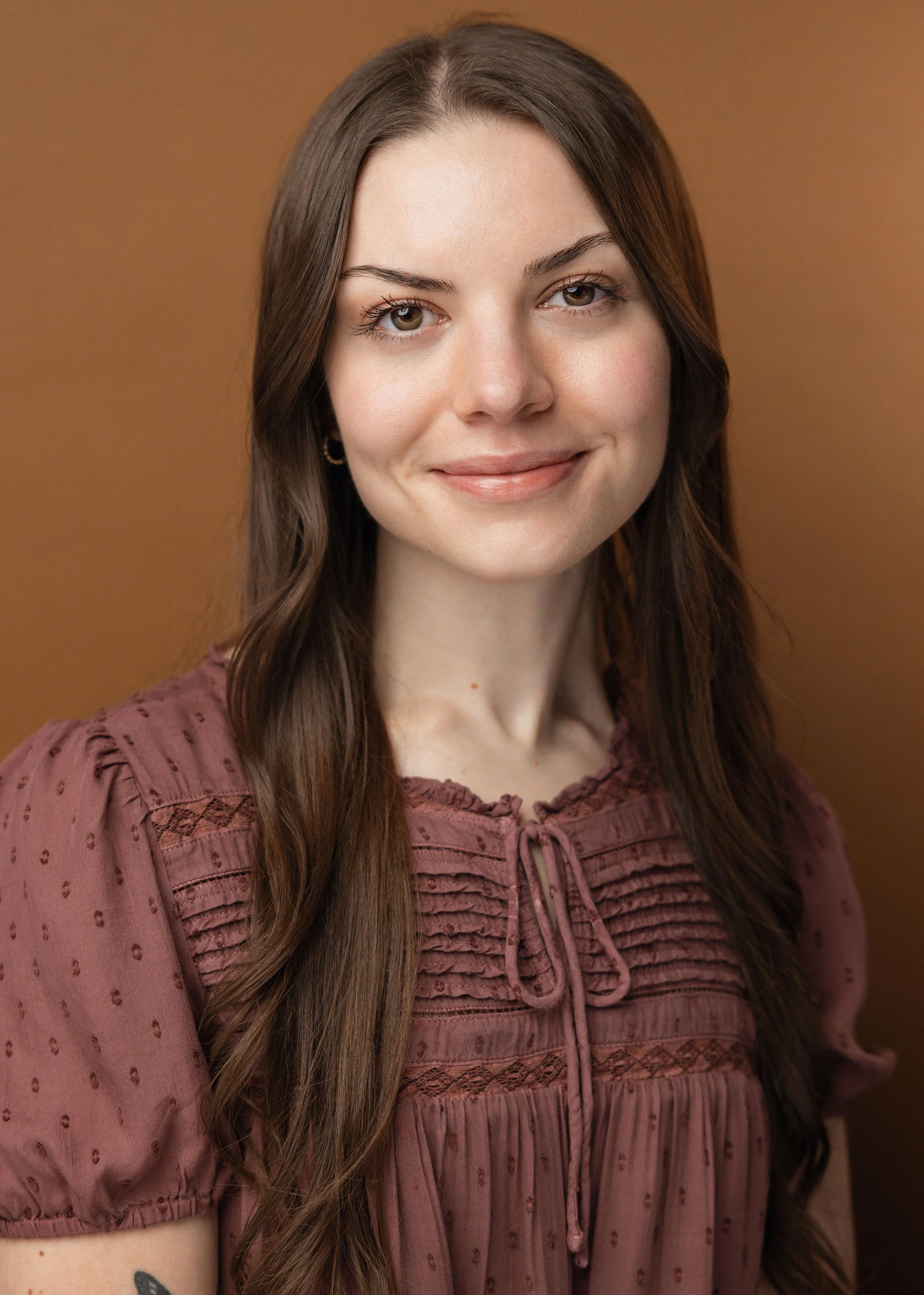 White woman with brown hair smiling set against a brown background