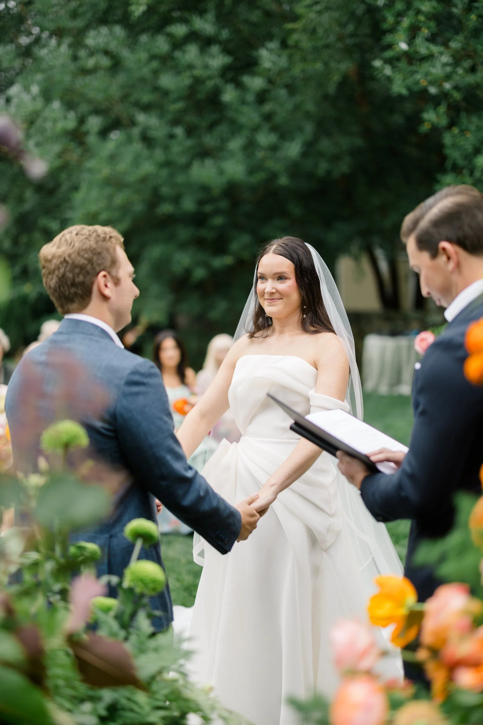 Bride and groom exchanging vows beneath a vibrant garden-inspired floral installation.