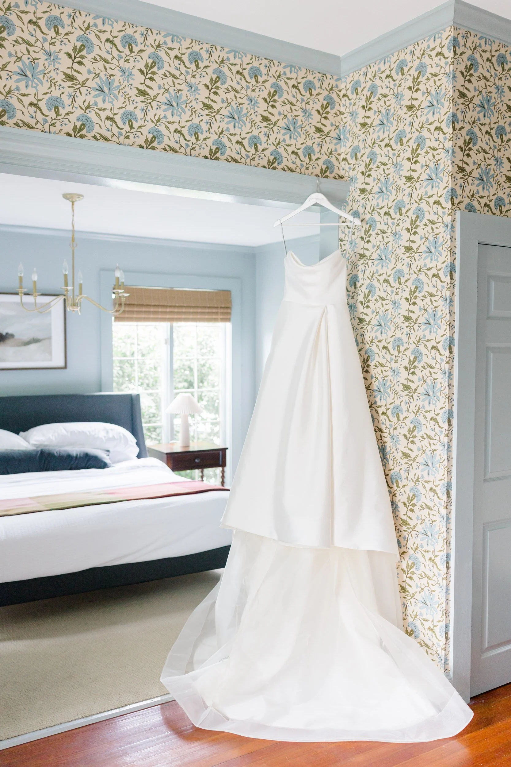The bride's Monique Lhuillier wedding dress hanging in natural light before her elegant Crane Estate wedding celebration.